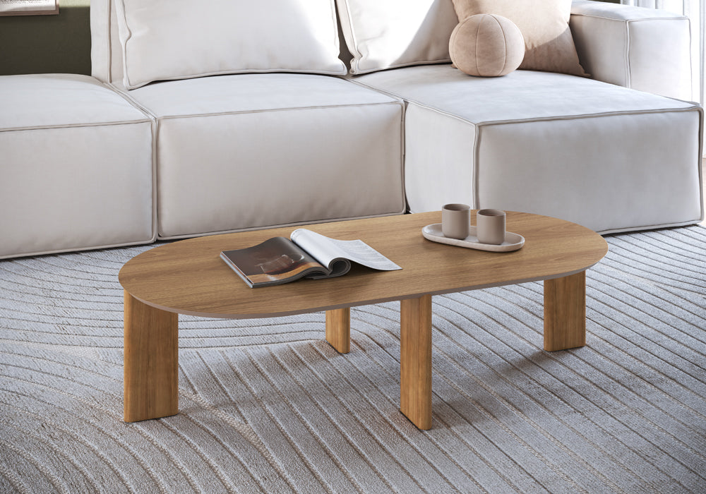 Mesa de centro oval amadeirada em sala de estar com sofá modular claro, tapete com relevo e revista aberta