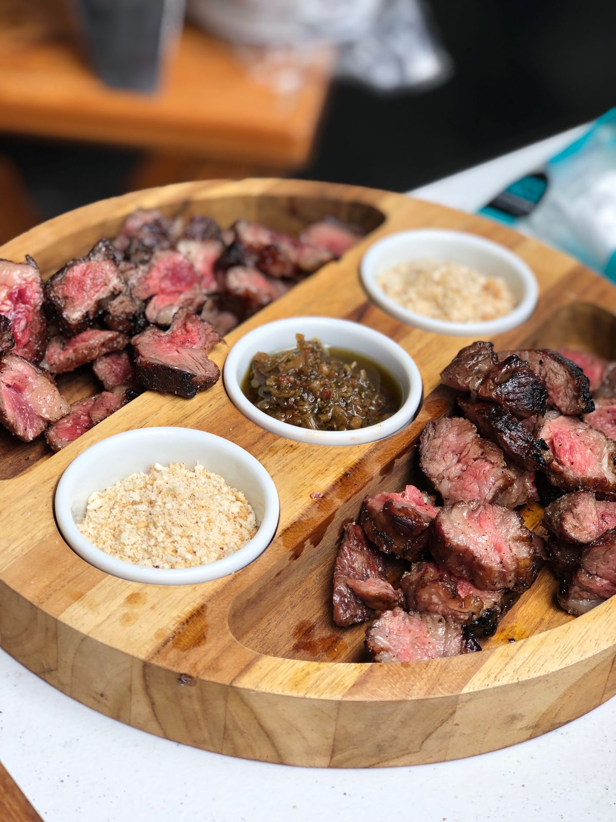 Petisqueira de teca maciça com potes de porcelana e porções de carne e molhos