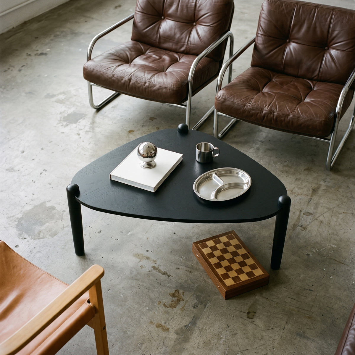 Mesa de centro no acabamento Nero em sala com poltronas de couro marrom e piso de cimento, vista superior