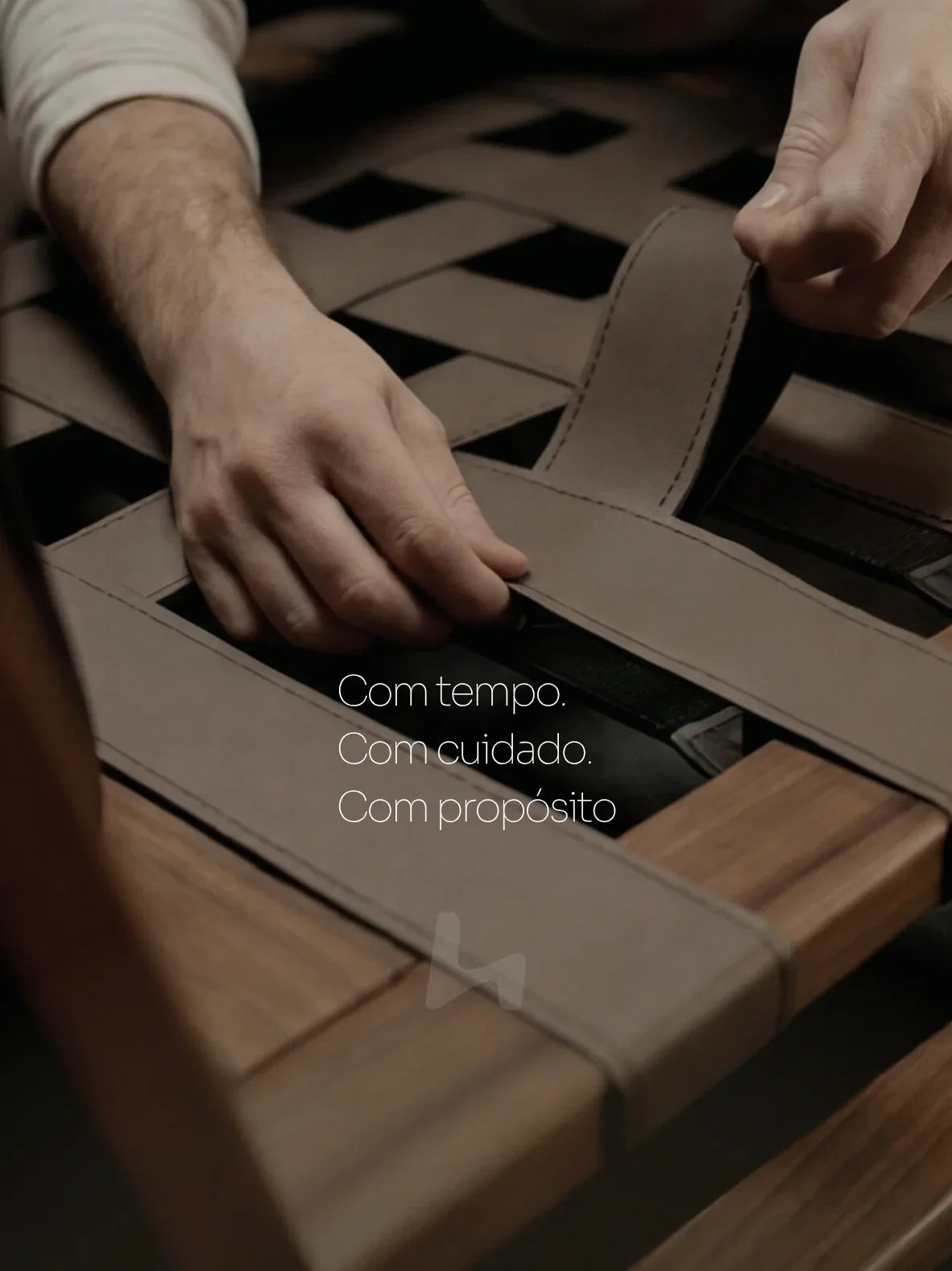 Mãos ajustando tiras de couro em estrutura de madeira, fabricação artesanal de móveis premium.