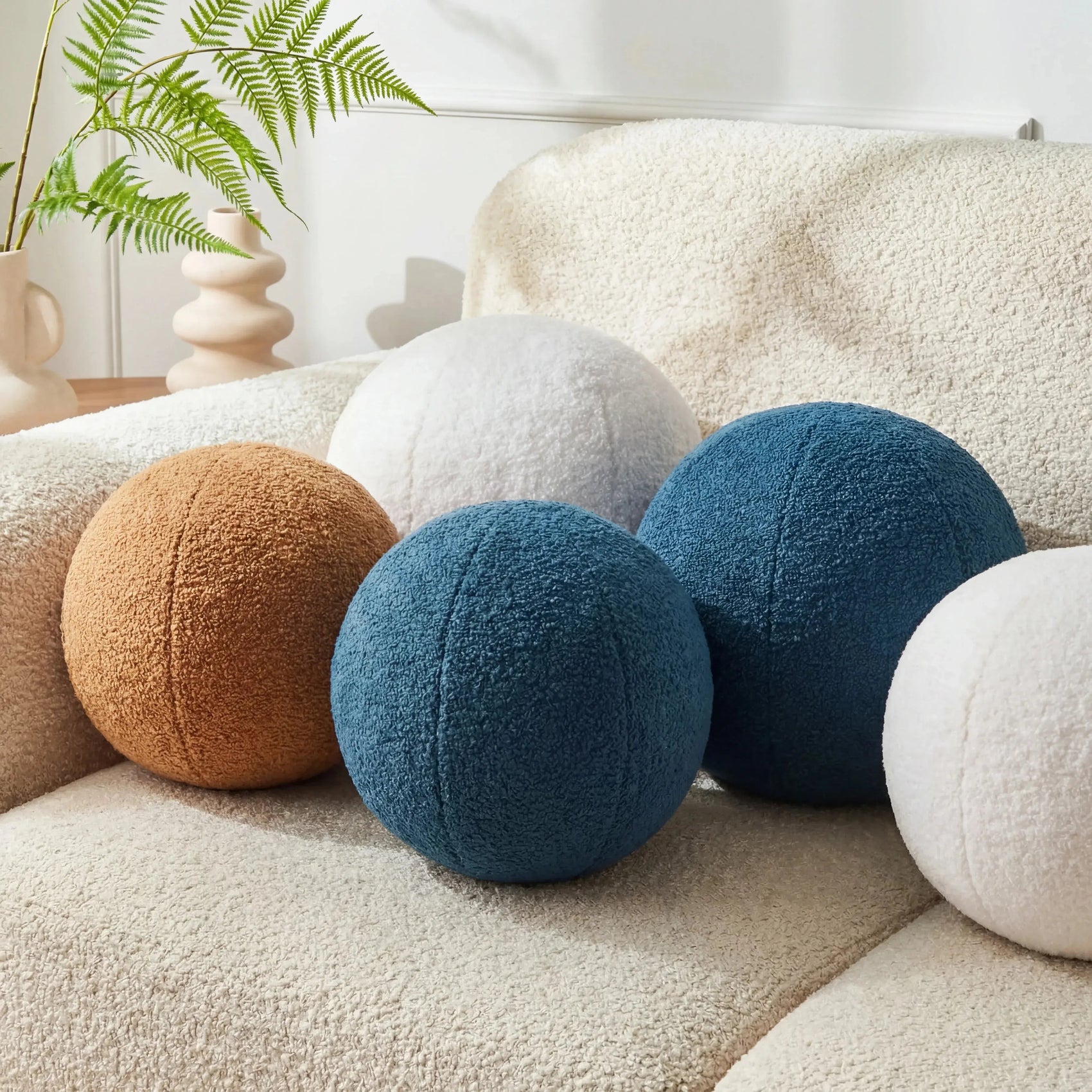 Almofadas decorativas redondas de pelúcia azul, branca e caramelo sobre sofá bege