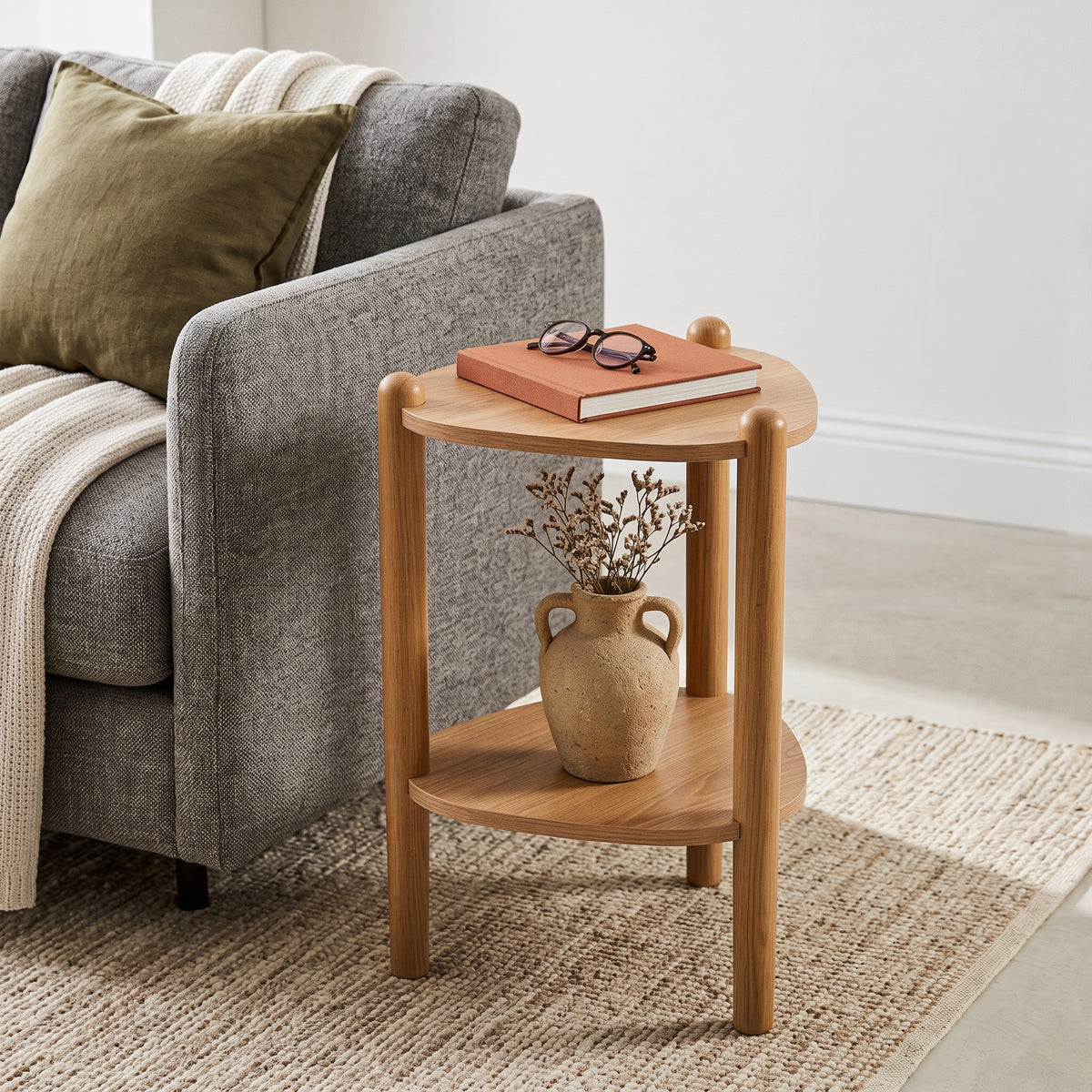 Mesa lateral ao lado de sofá cinza em sala de estar com livro e óculos no tampo e vaso na prateleira
