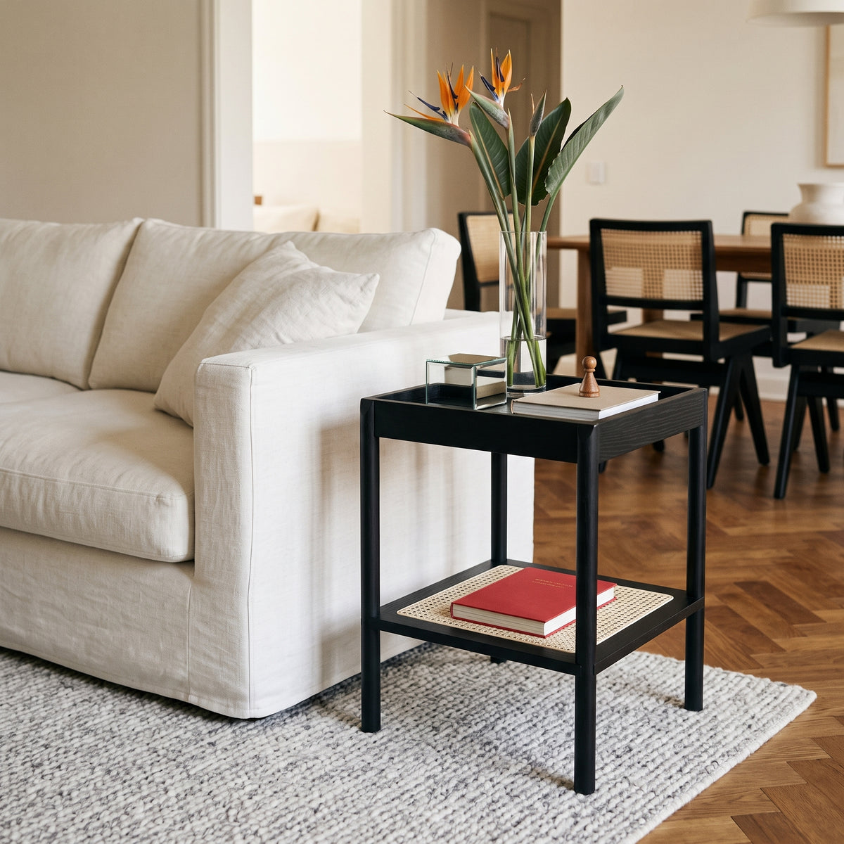 Mesa lateral no acabamento Nero em sala de estar com sofá claro, vaso de estrelícias e piso de tacos