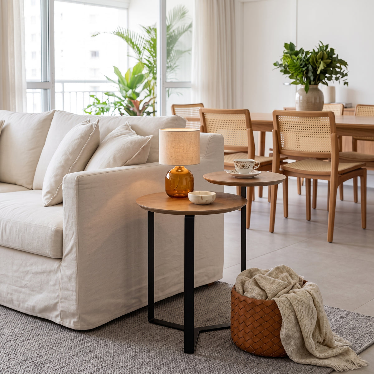 Mesa lateral de dois tampos em sala de estar com sofá claro, abajur âmbar e cesto trançado com manta