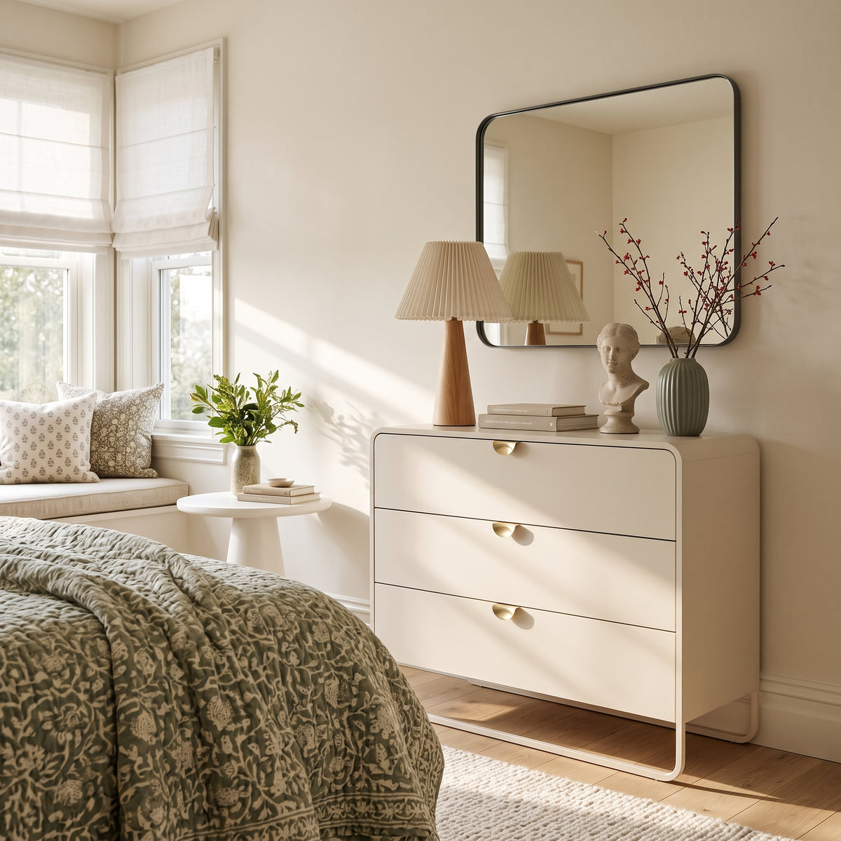 Cômoda offwhite em quarto com espelho na parede, abajur e cama com colcha estampada