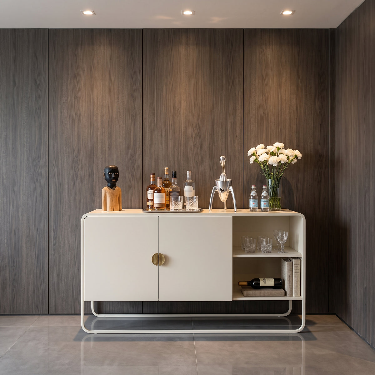 Balcão buffet offwhite em sala com painel escuro, garrafas, escultura e vaso de flores brancas
