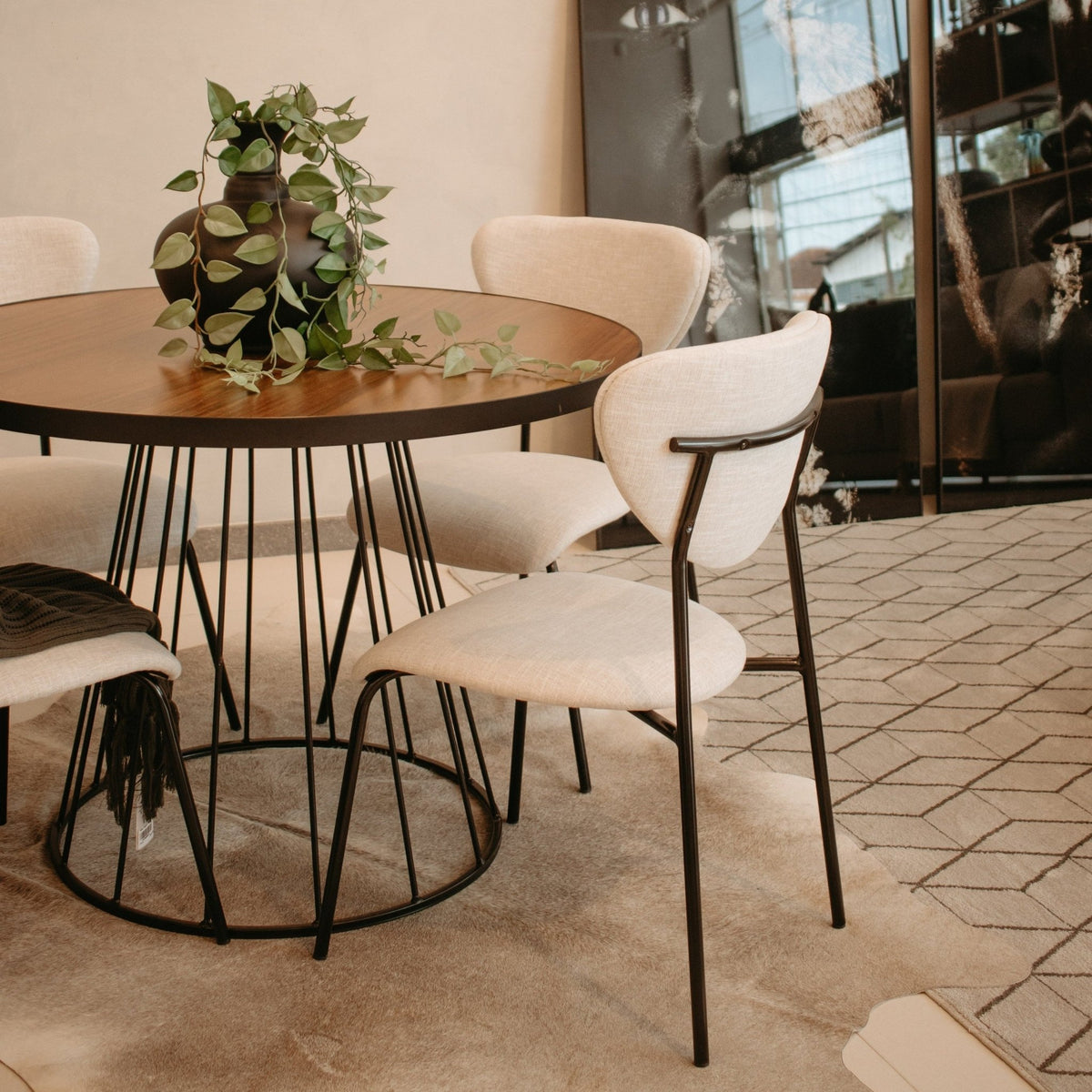 Cadeiras ao redor de mesa redonda de base aramada em sala de jantar com cristaleira e piso de ladrilho