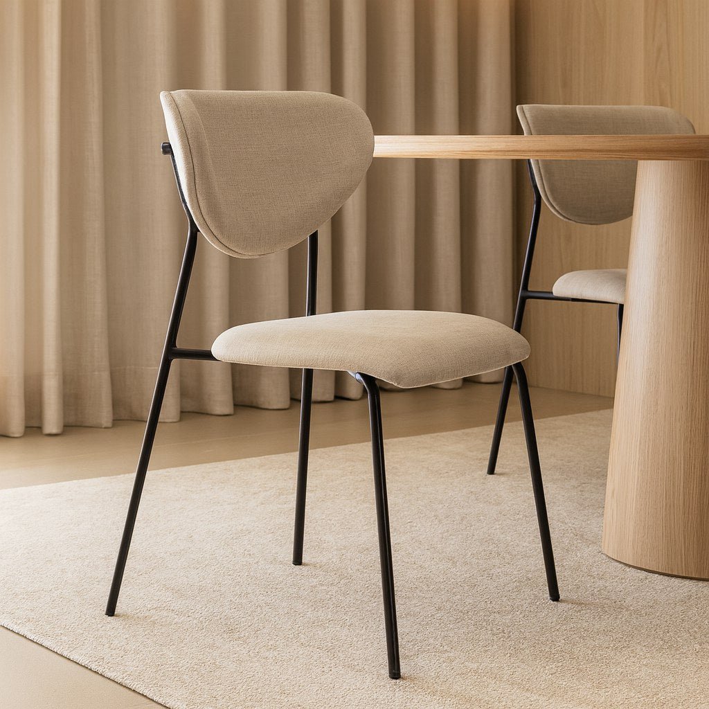 Cadeira de pés metálicos finos em sala de jantar com mesa redonda de madeira, cortina e tapete claro