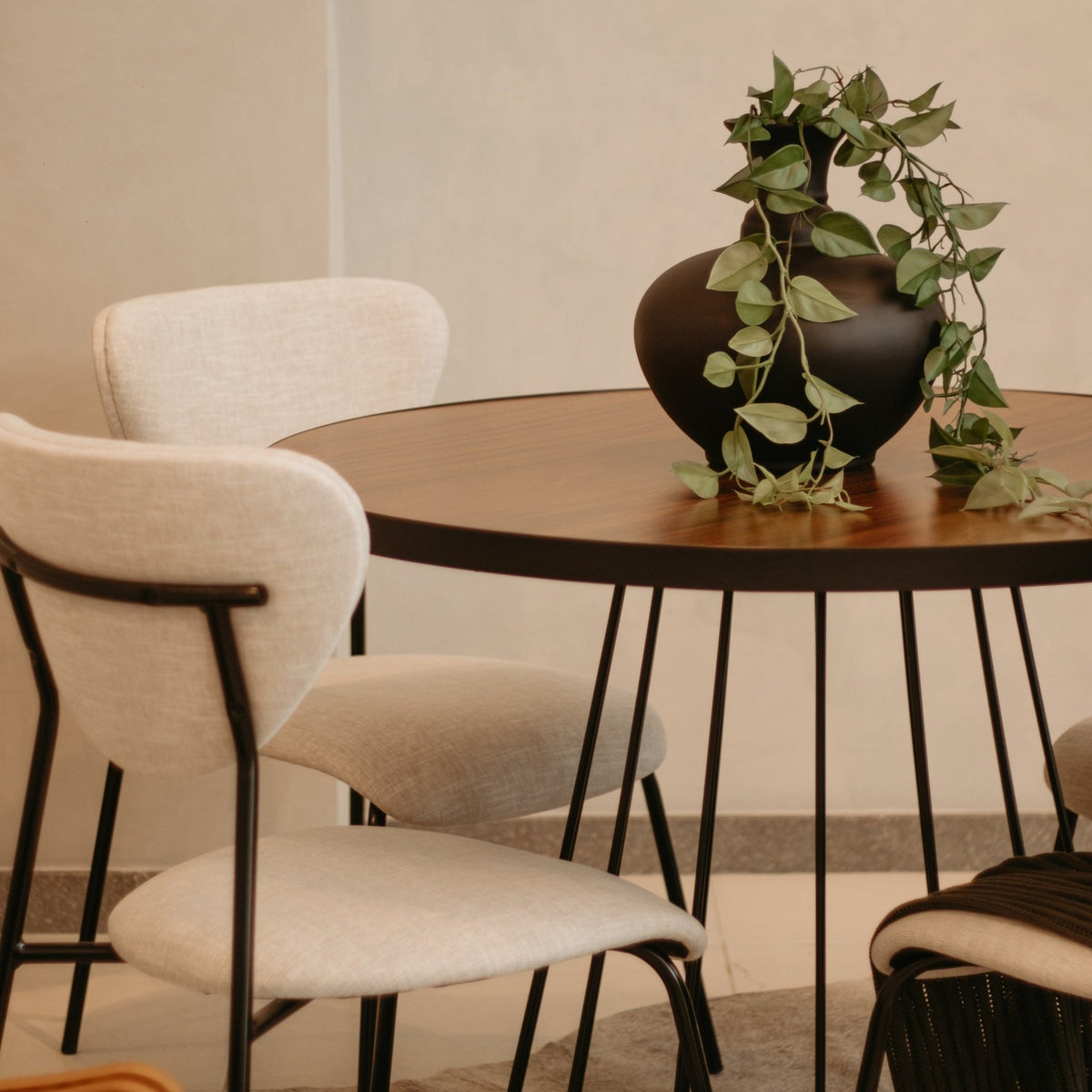 Cadeiras de tecido texturizado em sala de jantar com mesa redonda de base aramada e vaso com planta