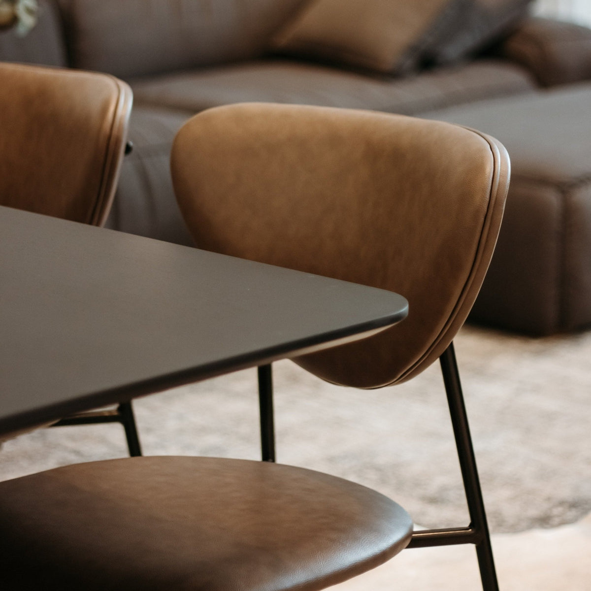 Cadeira de encosto em concha e revestimento liso em sala de jantar com mesa de tampo escuro e sofá ao fundo