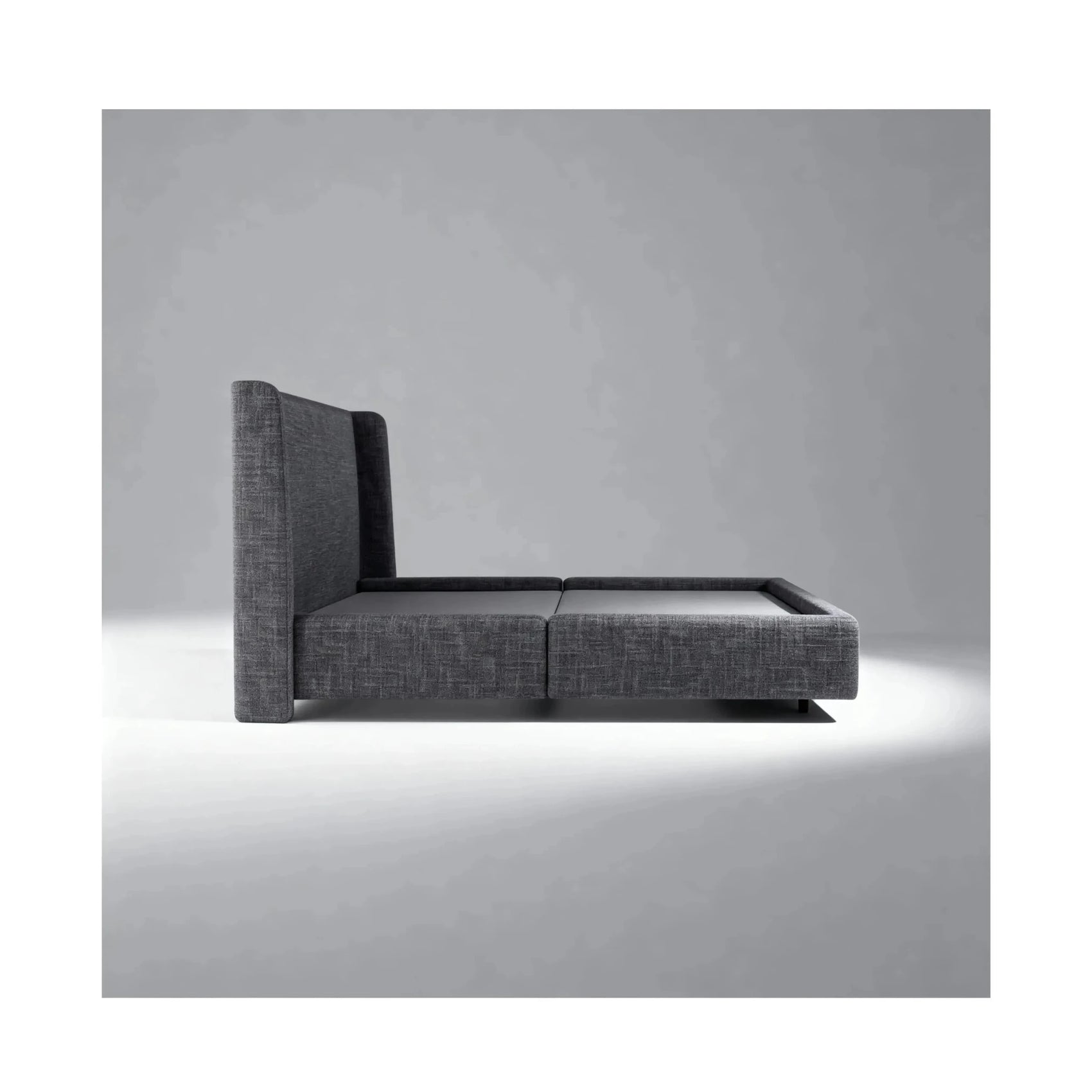 Cama estofada cinza com cabeceira e apoio lateral, vista lateral com acabamento preto