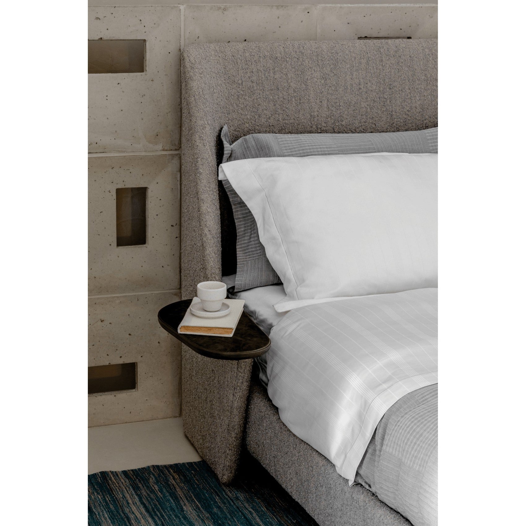 Cama Aura estofada cinza, lateral alta e roupa de cama branca com detalhe listrado