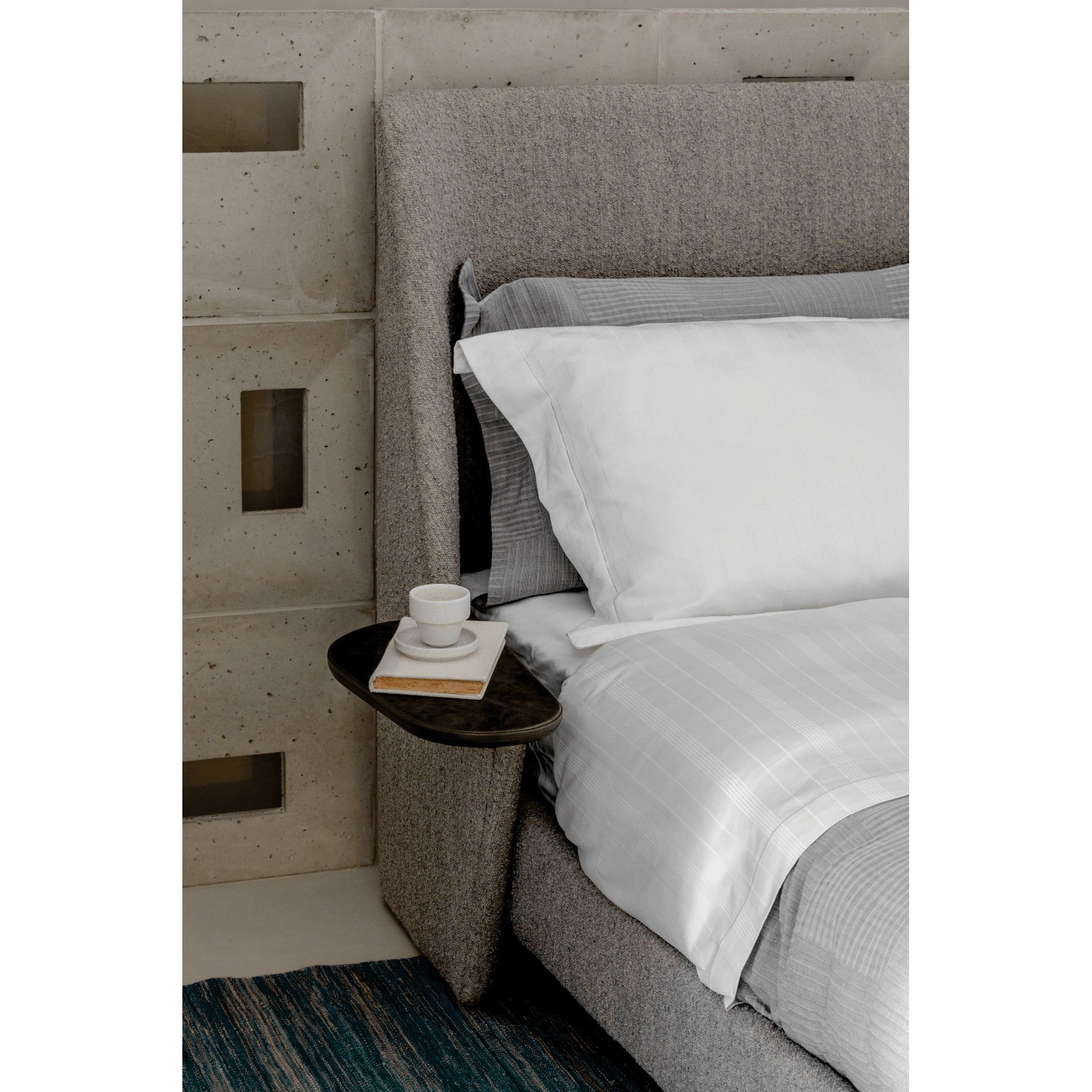 Cama Aura estofada cinza, lateral alta e roupa de cama branca com detalhe listrado