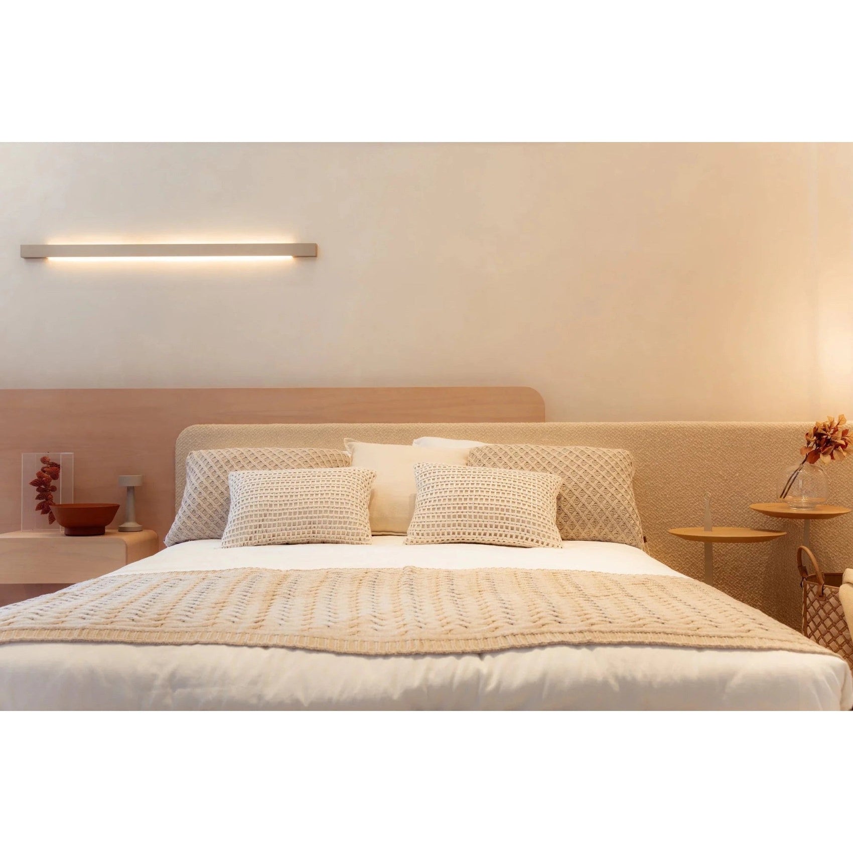 Cama estofada bege com cabeceira alta, almofadas e colcha branca com faixa