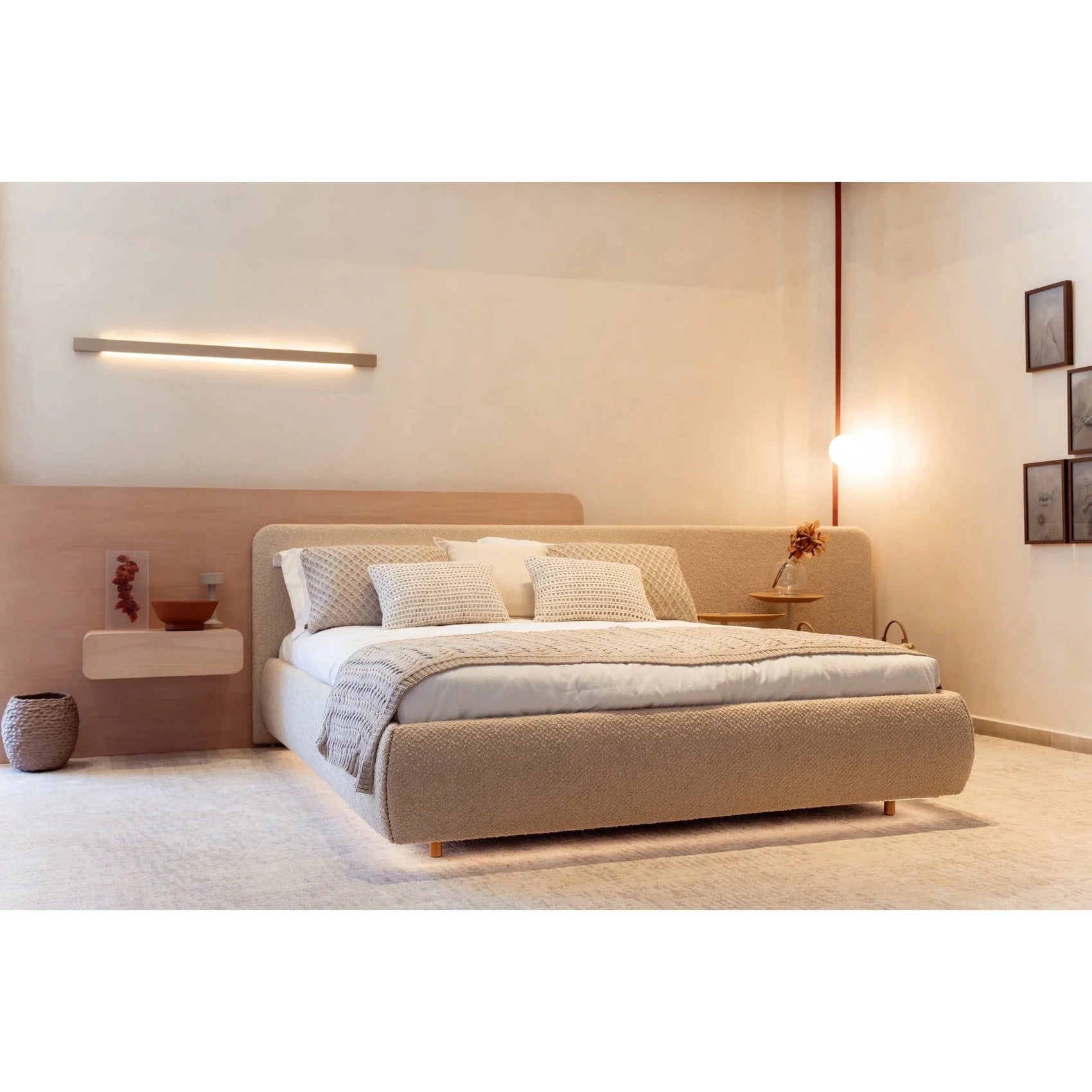 Cama estofada bege com almofadas claras e colcha sobre base retangular