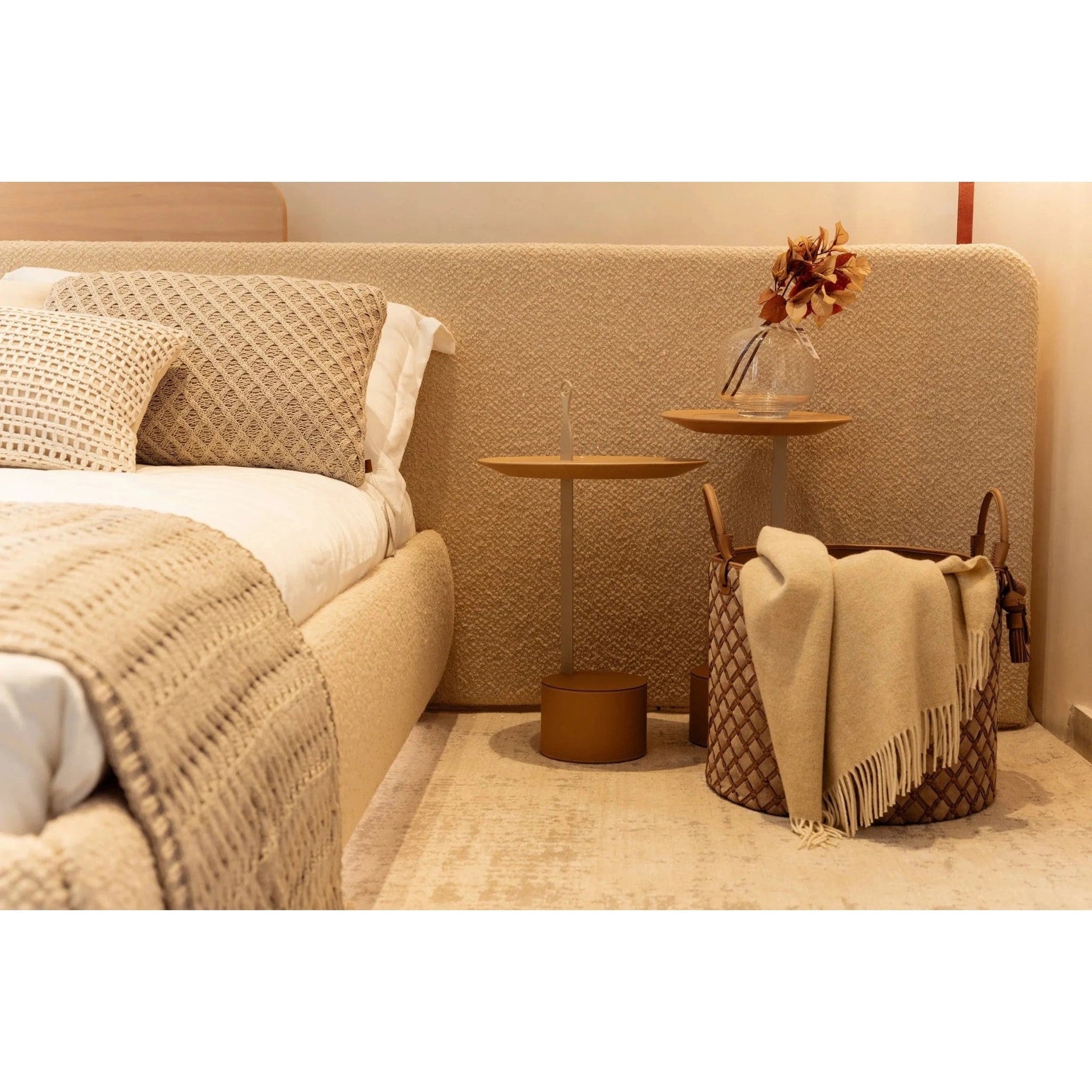 Cama estofada bege com almofadas claras e manta branca trançada