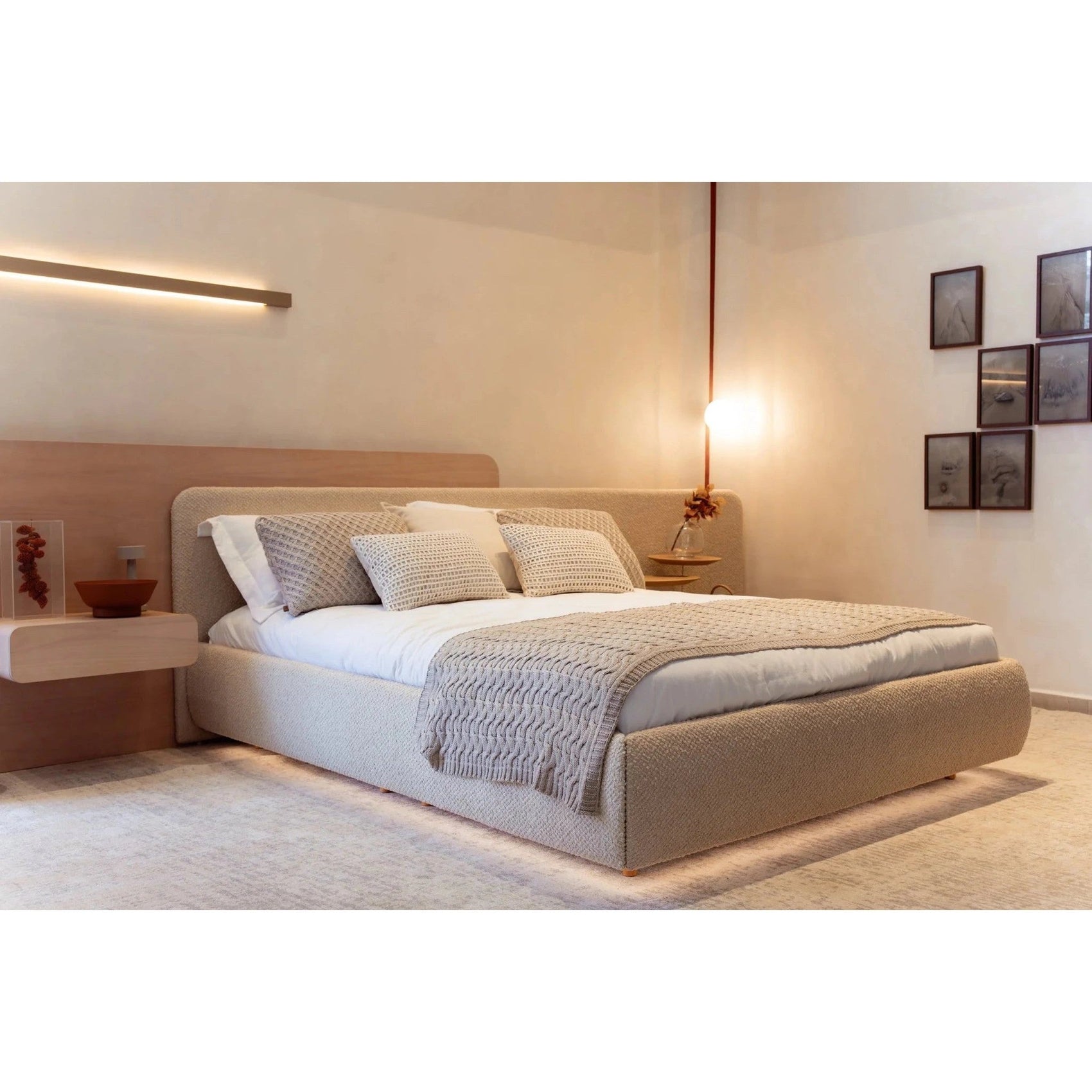 Cama estofada bege com almofadas claras e manta trançada sobre a cama