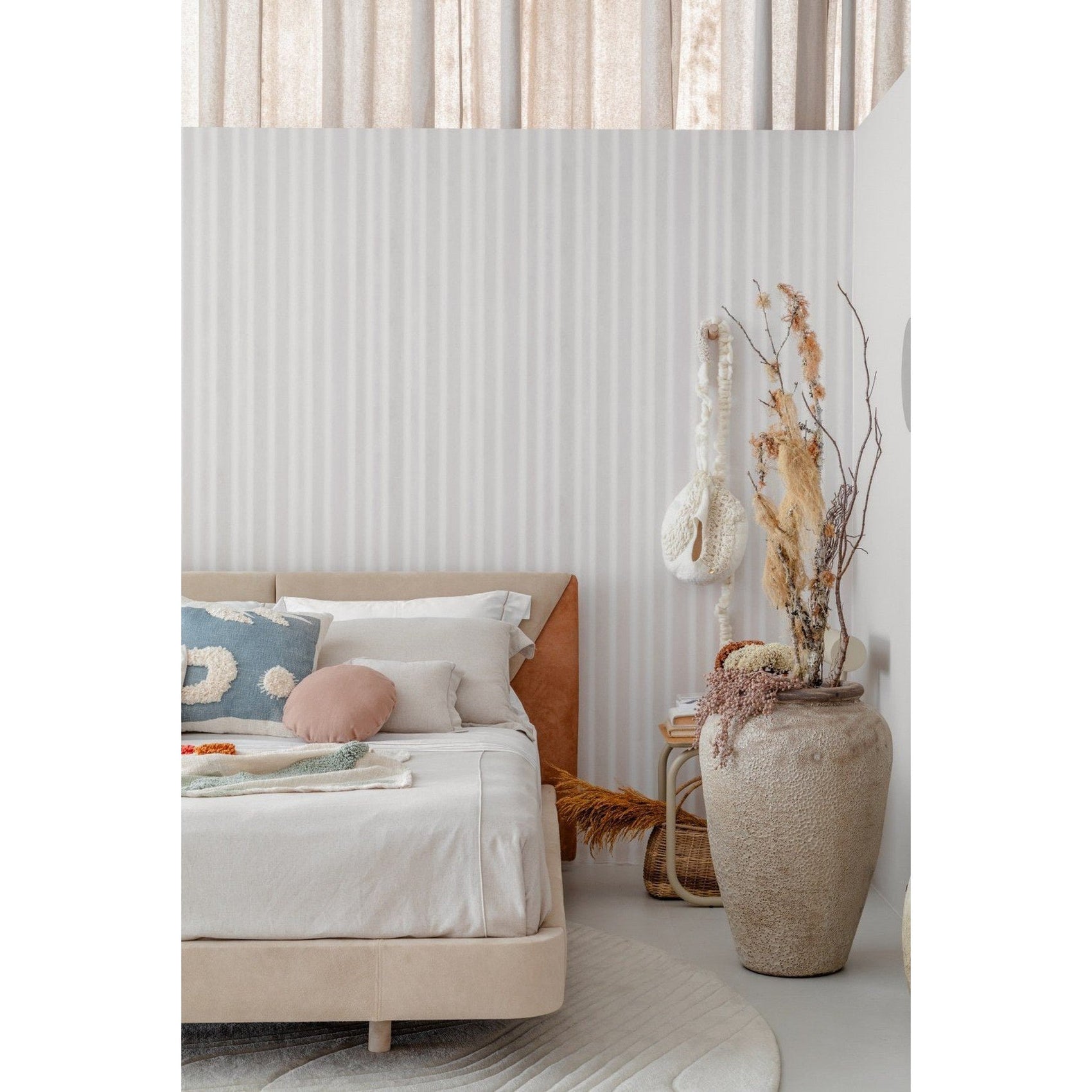 Cama estofada bege com cabeceira alta, roupa de cama branca e almofadas decorativas.