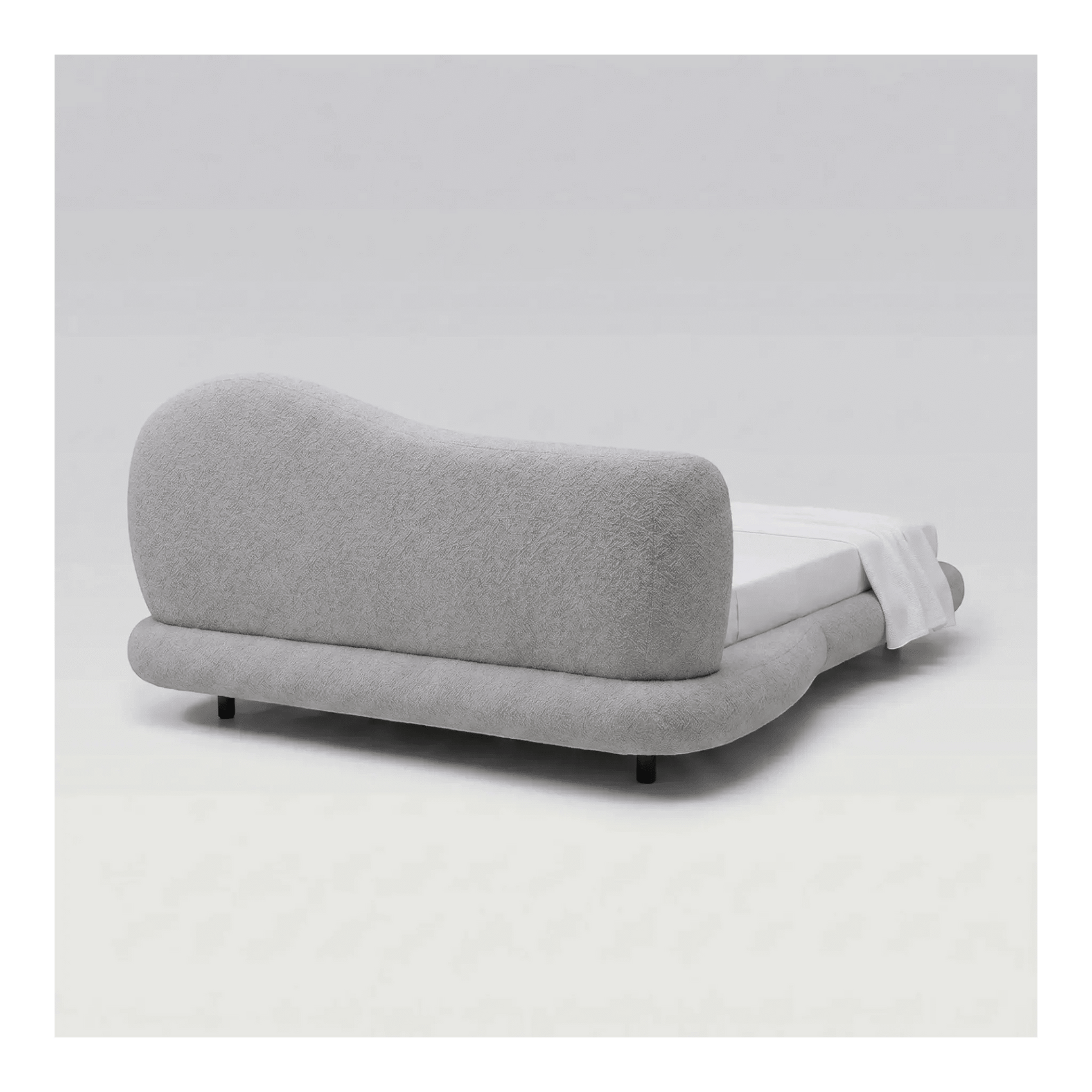 Cama estofada cinza perfil lateral, cabeceira curva alta e travesseiros brancos.