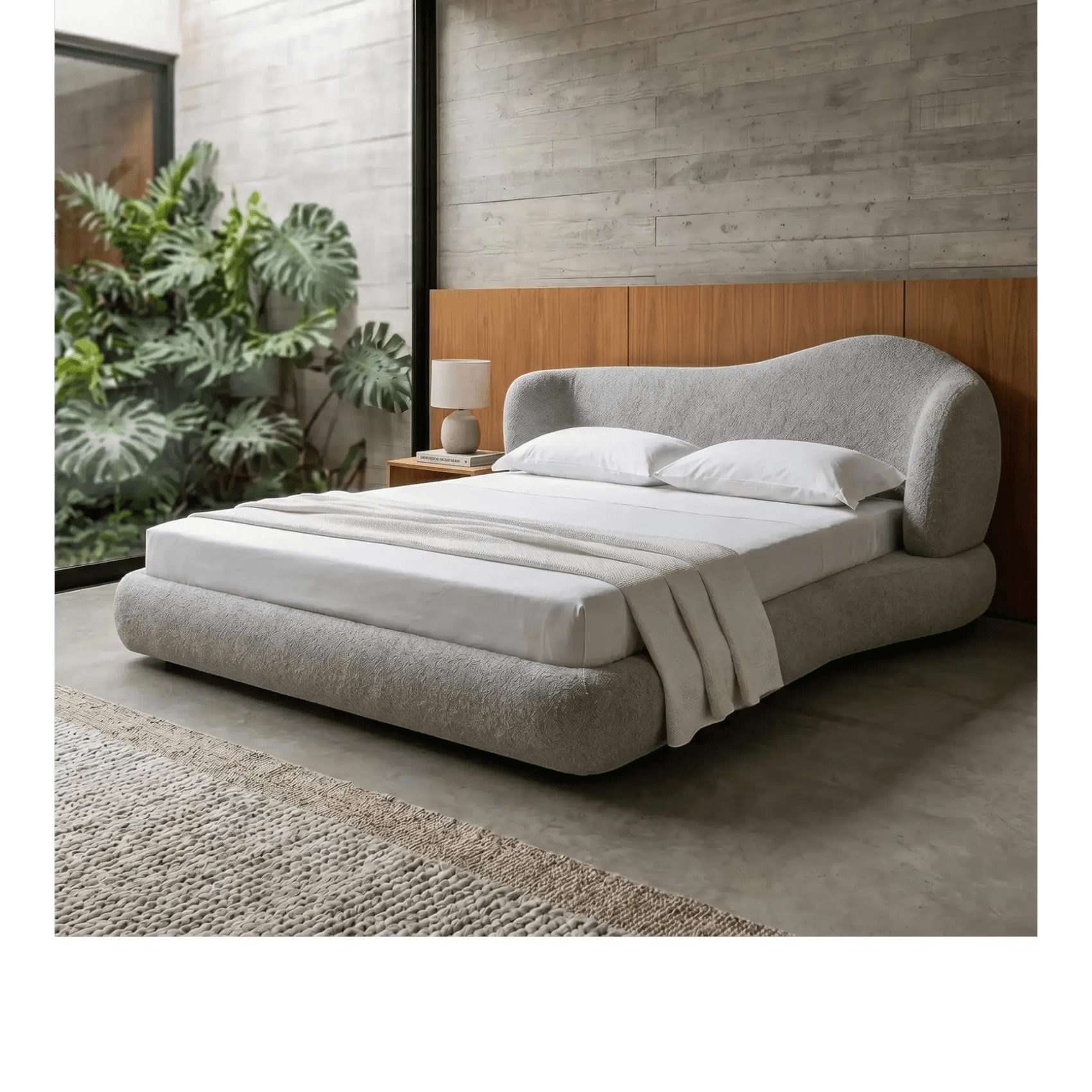 Cama estofada cinza com cabeceira curva, lençóis e travesseiros brancos.
