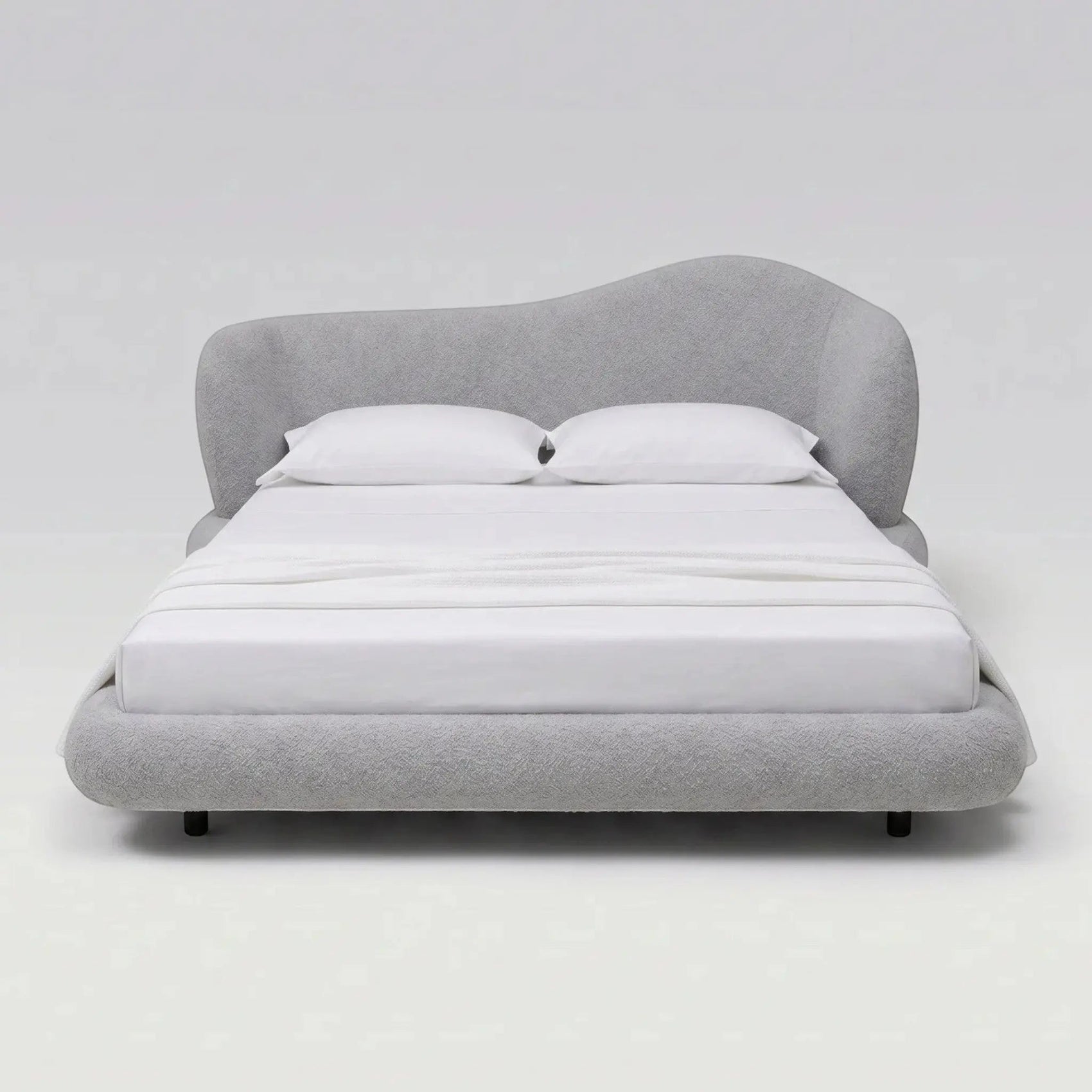 Cama estofada cinza vista de frente, com cabeceira alta arredondada e travesseiros brancos.