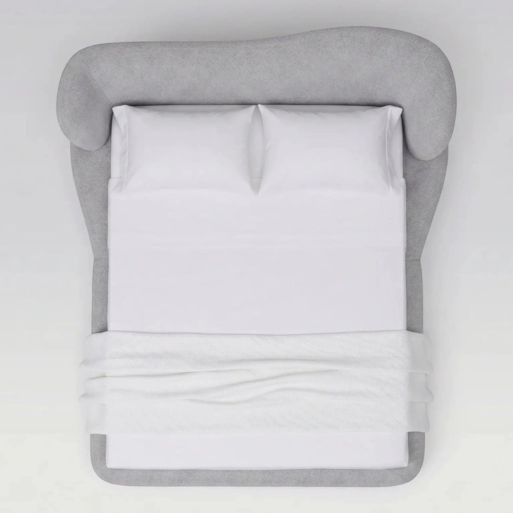 Cama estofada cinza vista frontal, com travesseiros brancos e lençol dobrado.