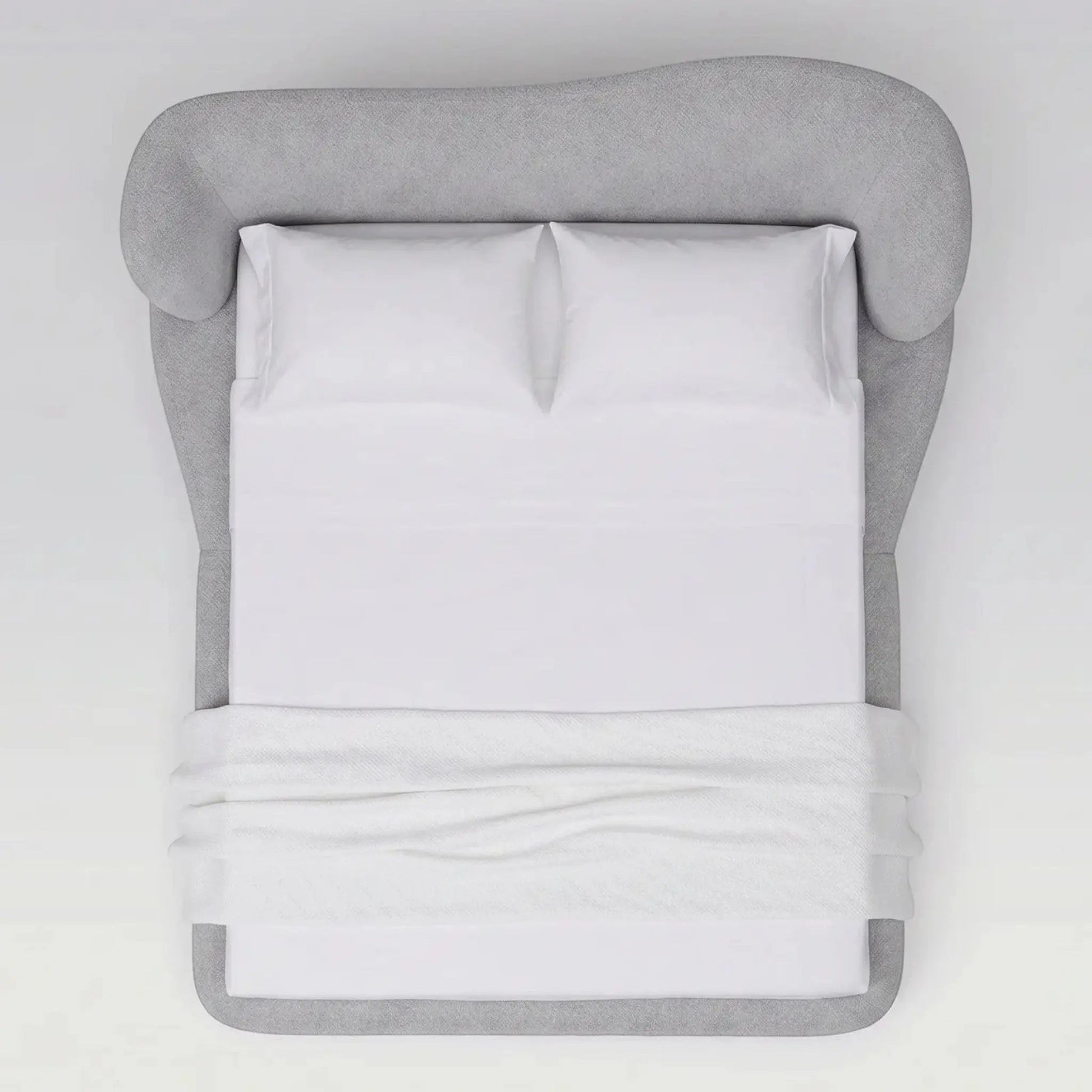 Cama estofada cinza vista frontal, com travesseiros brancos e lençol dobrado.
