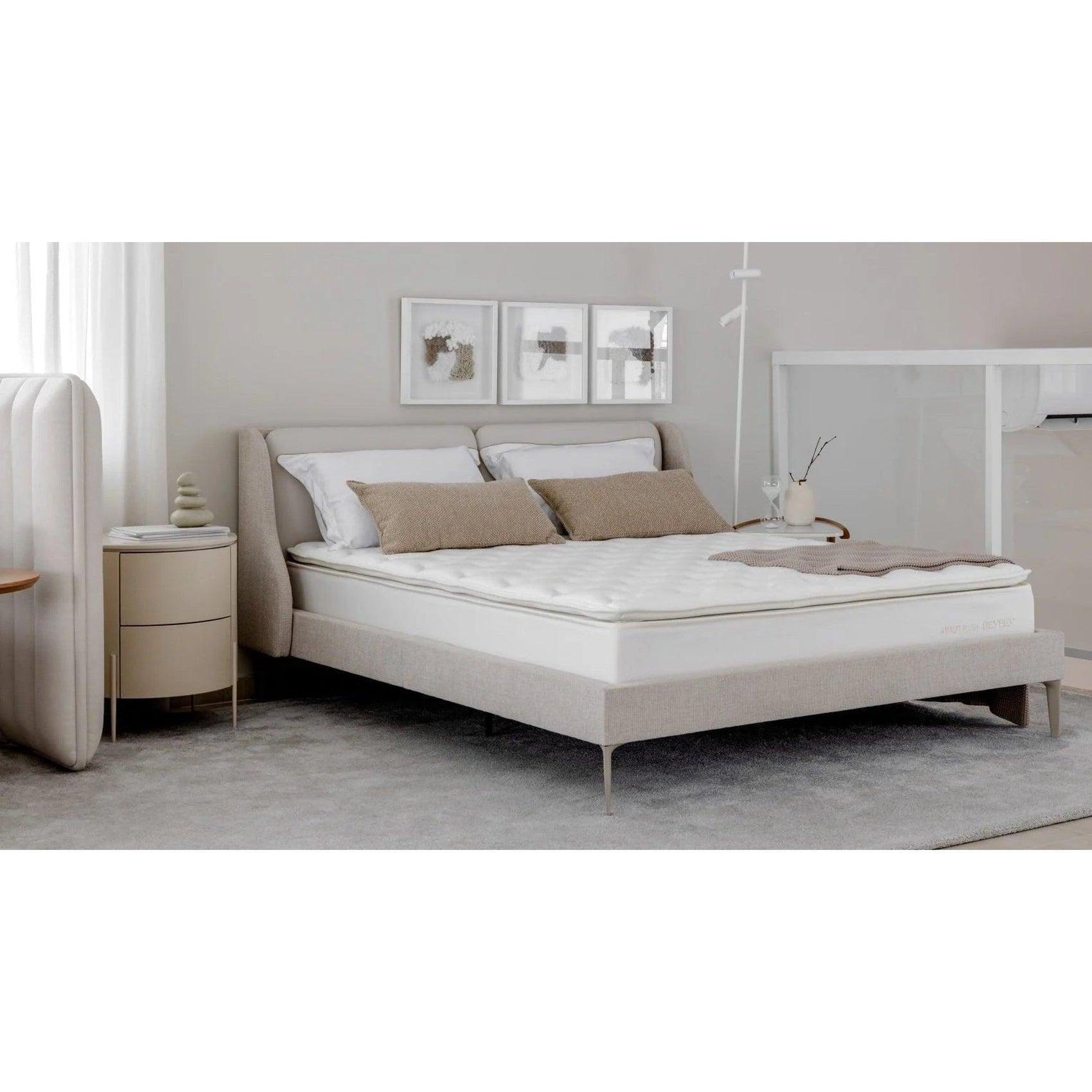 Cama com estrutura estofada bege, base suspensa e roupa de cama branca com almofadas bege.