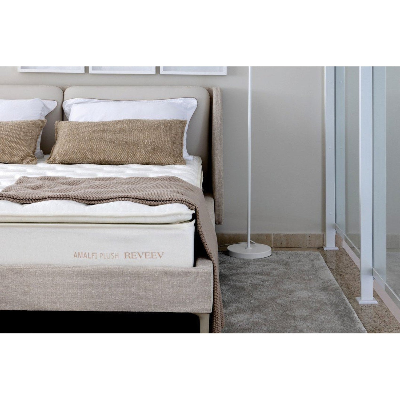 Cama estofada com travesseiros brancos e almofada bege texturizada, com manta dobrada bege.