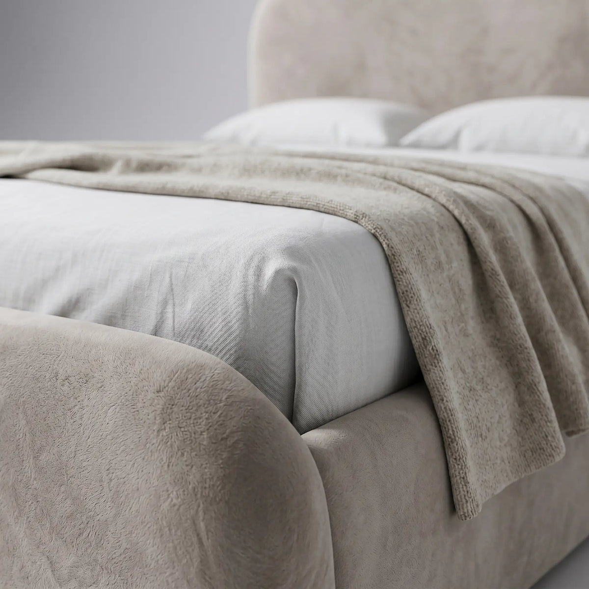 Detalhe da cama estofada clara com manta e tecido de revestimento visível na lateral