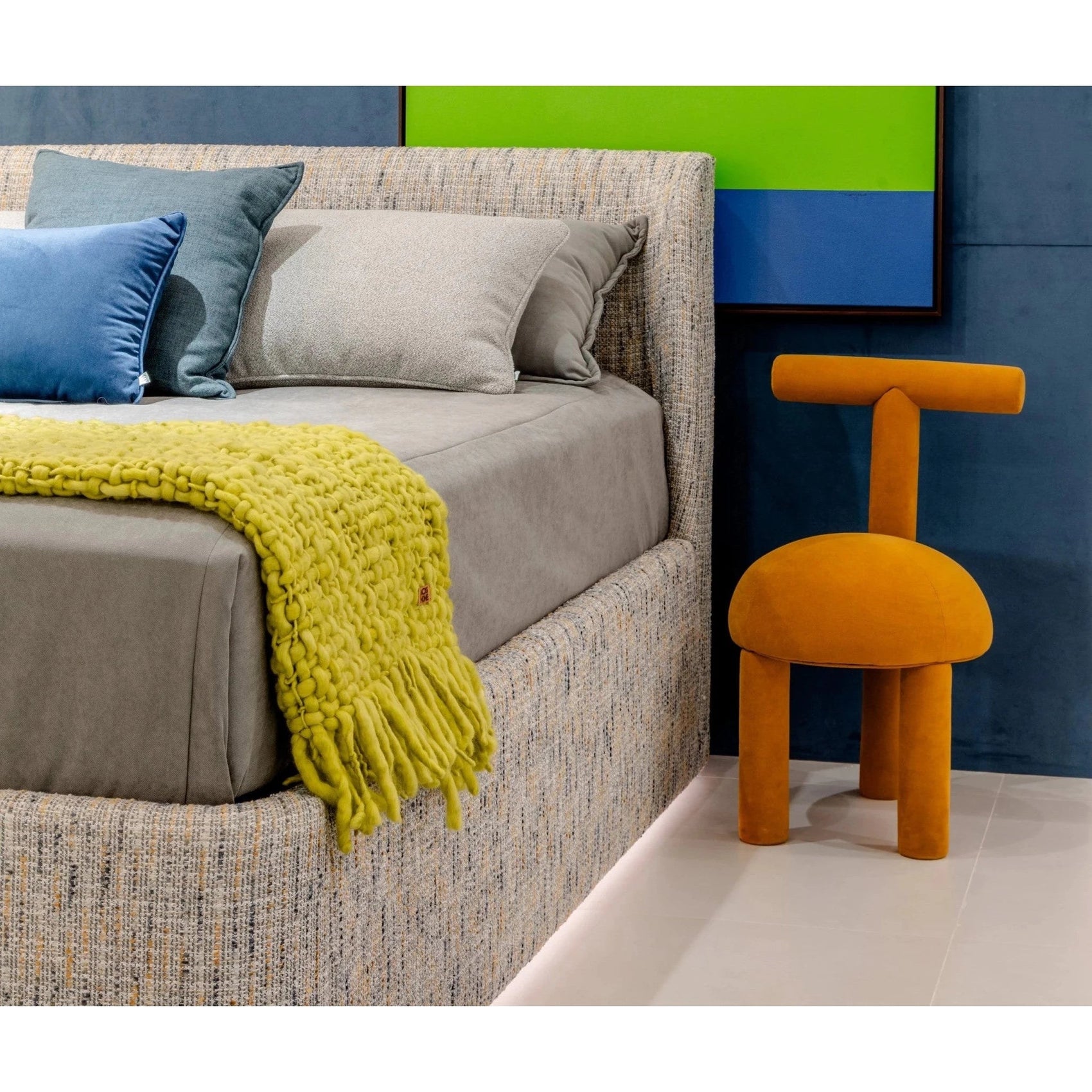 Cama estofada cinza com almofadas, manta amarela e encosto alto