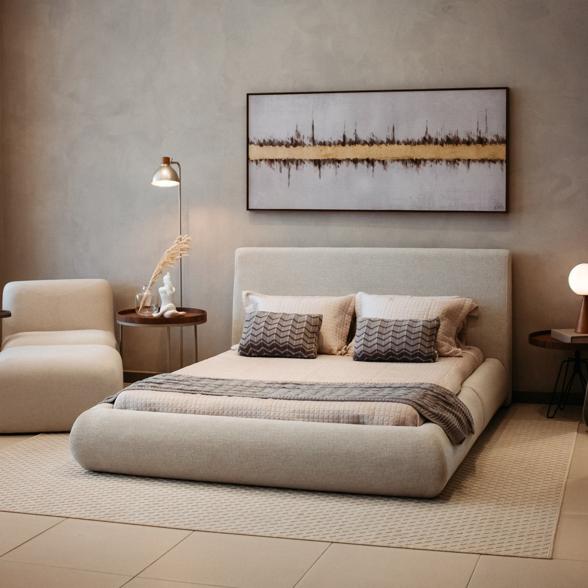Cama estofada em quarto com quadro horizontal, poltrona e luminária de piso