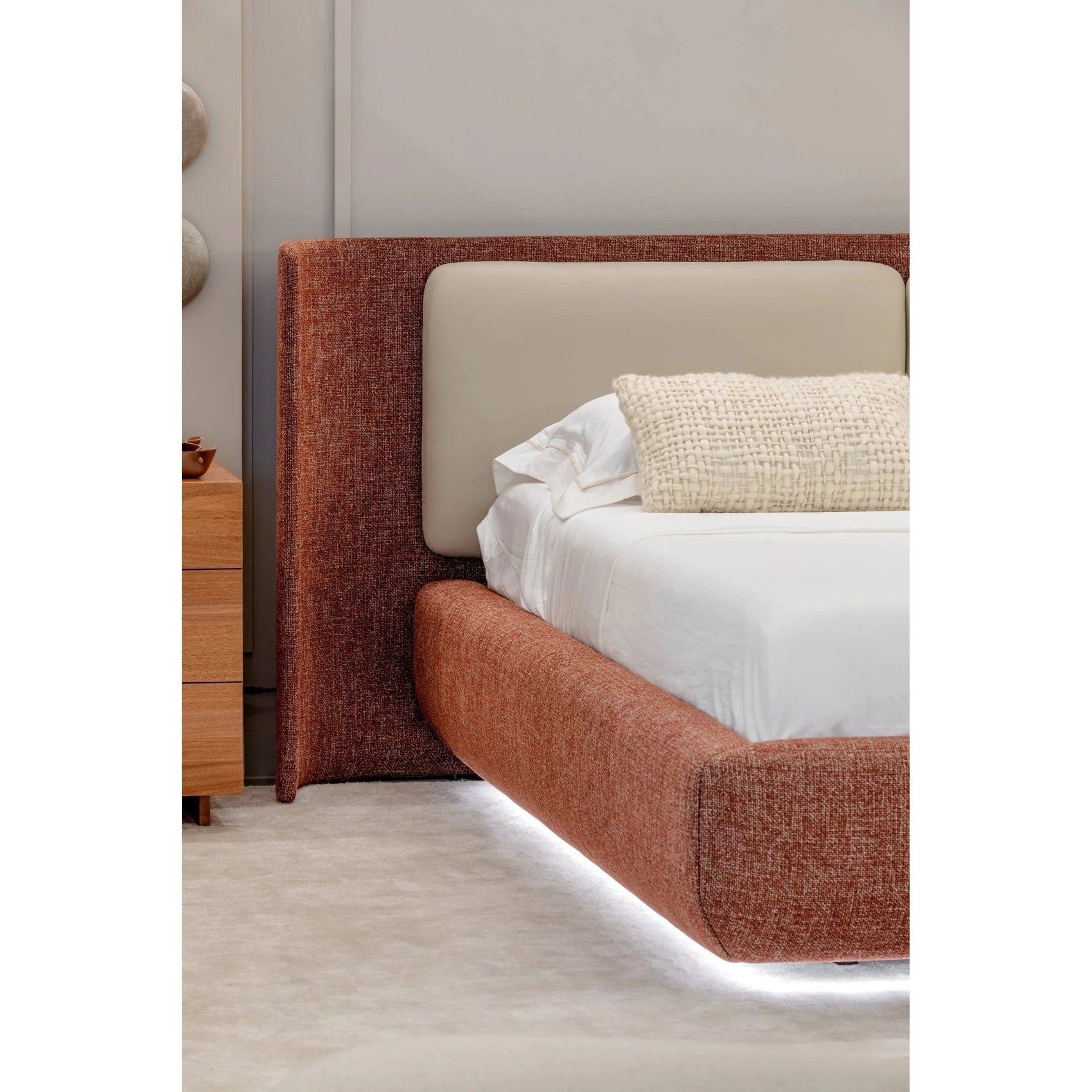 Cama estofada marrom com cabeceira e encosto alto, roupa de cama branca e almofadas claras
