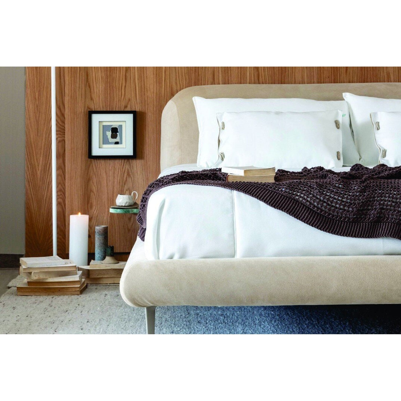 Cama estofada bege com travesseiros brancos e manta texturizada escura na parte da frente