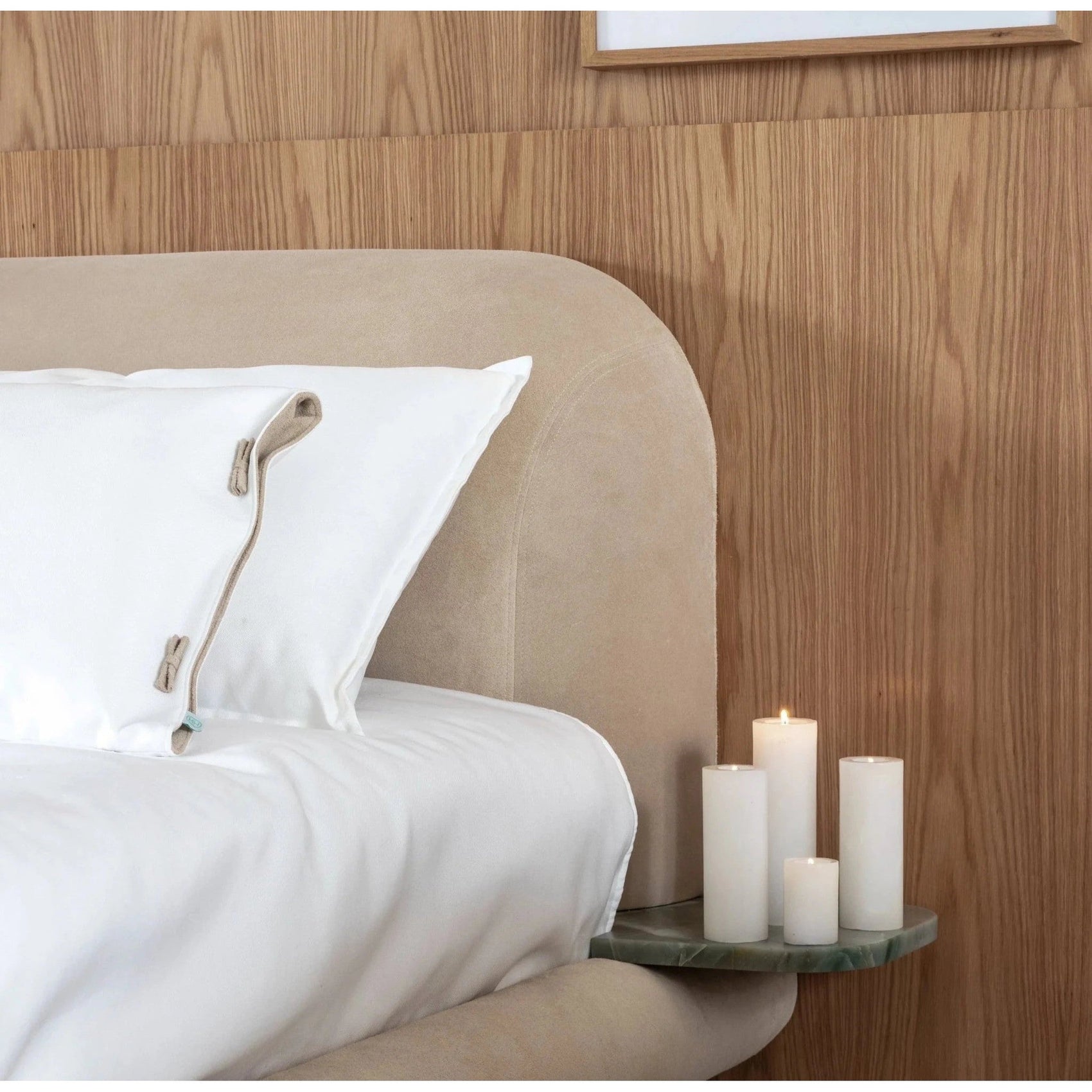 Cama estofada bege com roupa de cama branca e cabeceira arredondada, detalhe do travesseiro