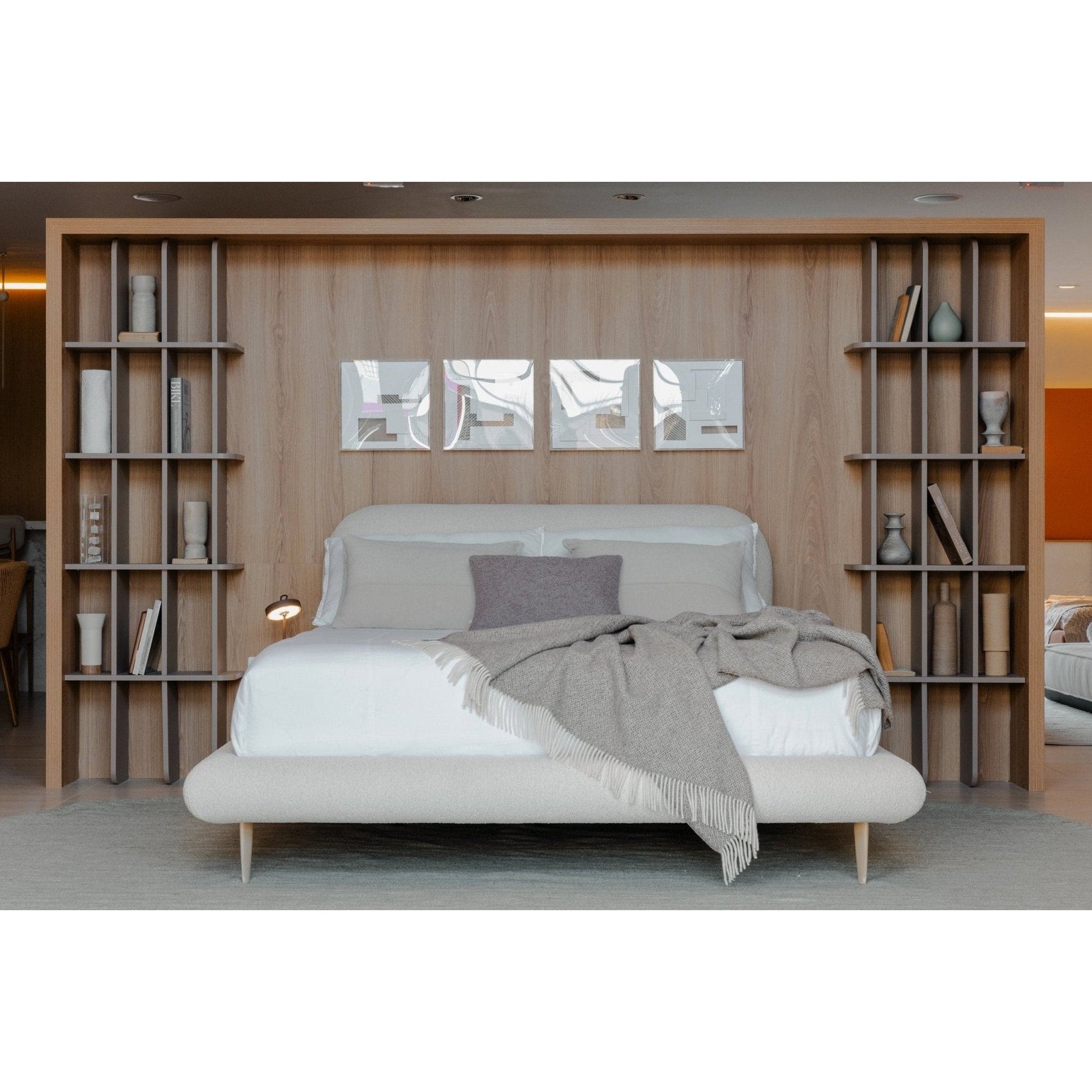 Cama estofada bege com conjunto de roupa de cama clara, travesseiros e manta sobre o colchão