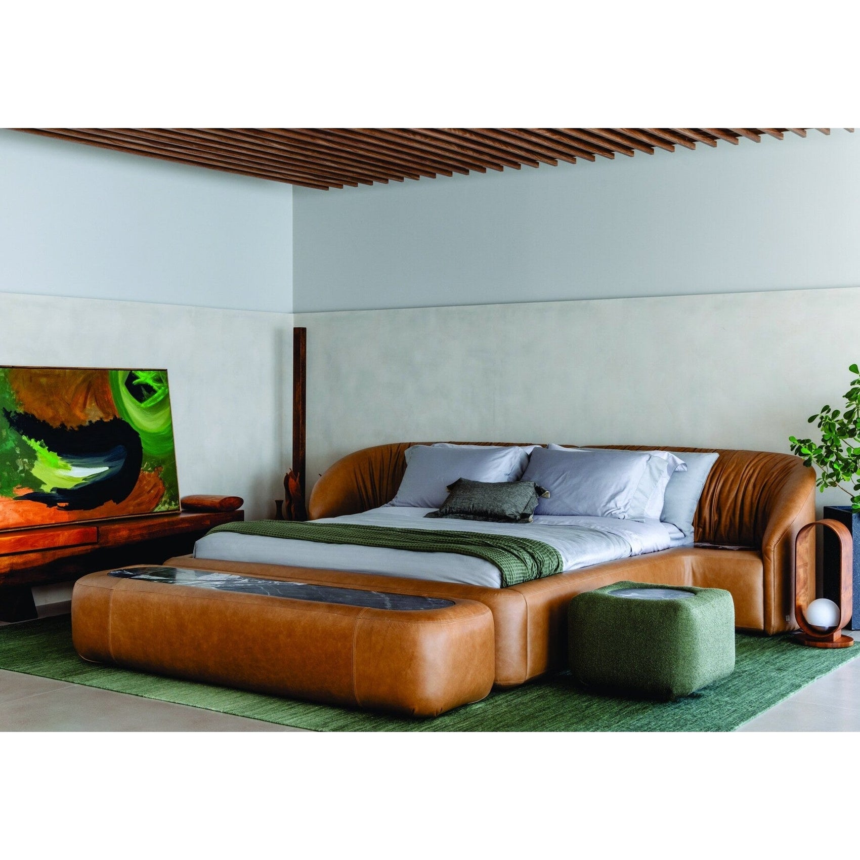 Cama estofada marrom com travesseiros cinza e manta verde, vista frontal em ângulo.
