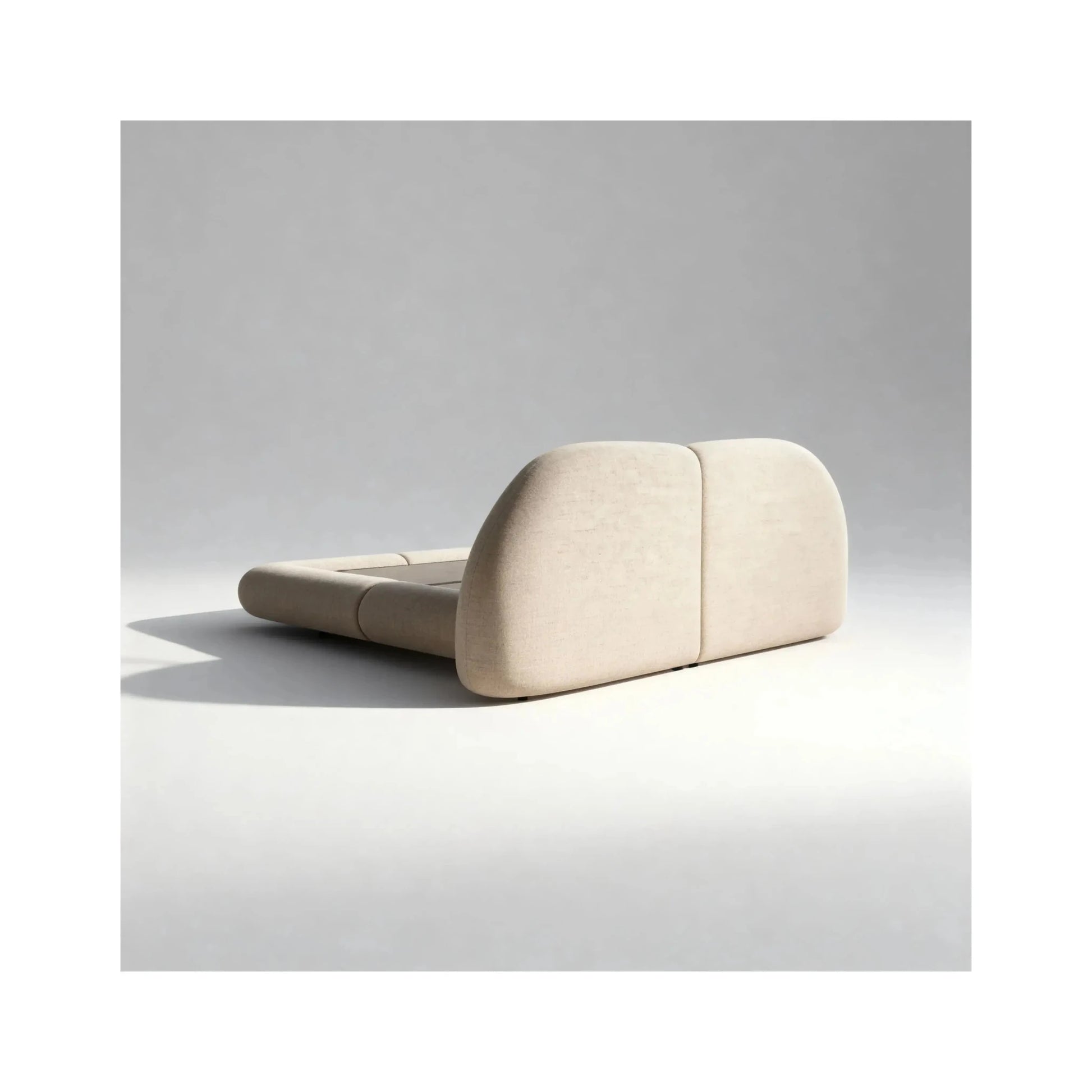 Cama estofada clara com cabeceira semicircular e base baixa acolchoada.