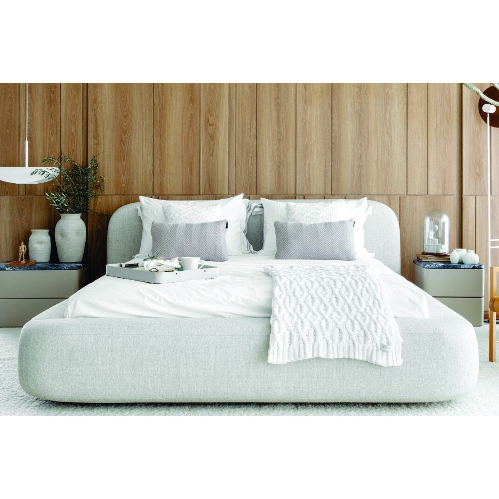 Cama estofada cinza claro com roupa de cama branca e colcha clara