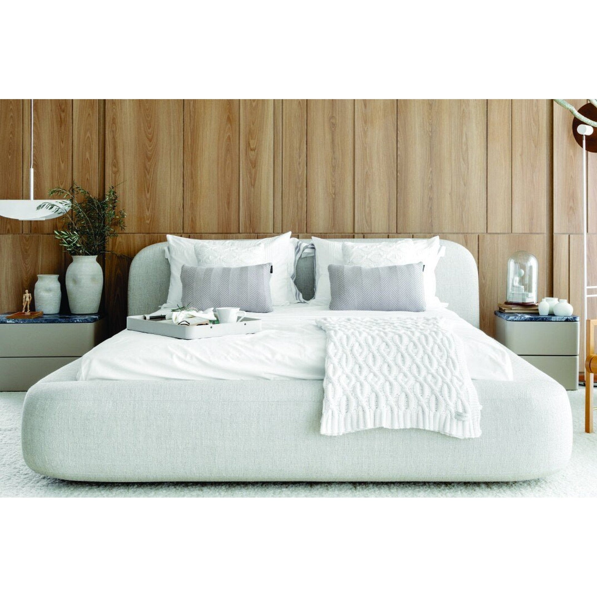 Cama estofada cinza claro com roupa de cama branca e colcha clara