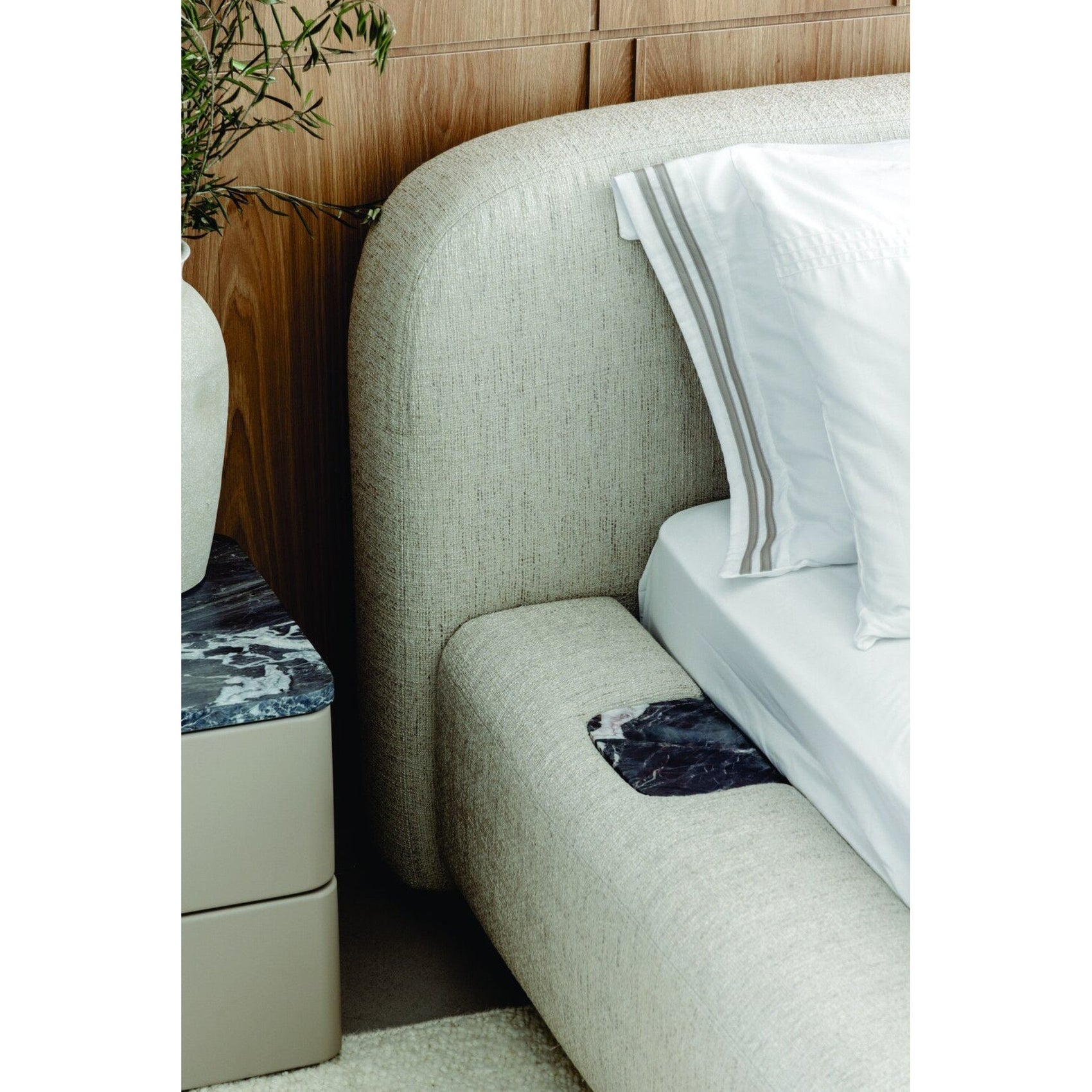 Cama estofada cinza claro com detalhe da cabeceira curvada e lençol branco