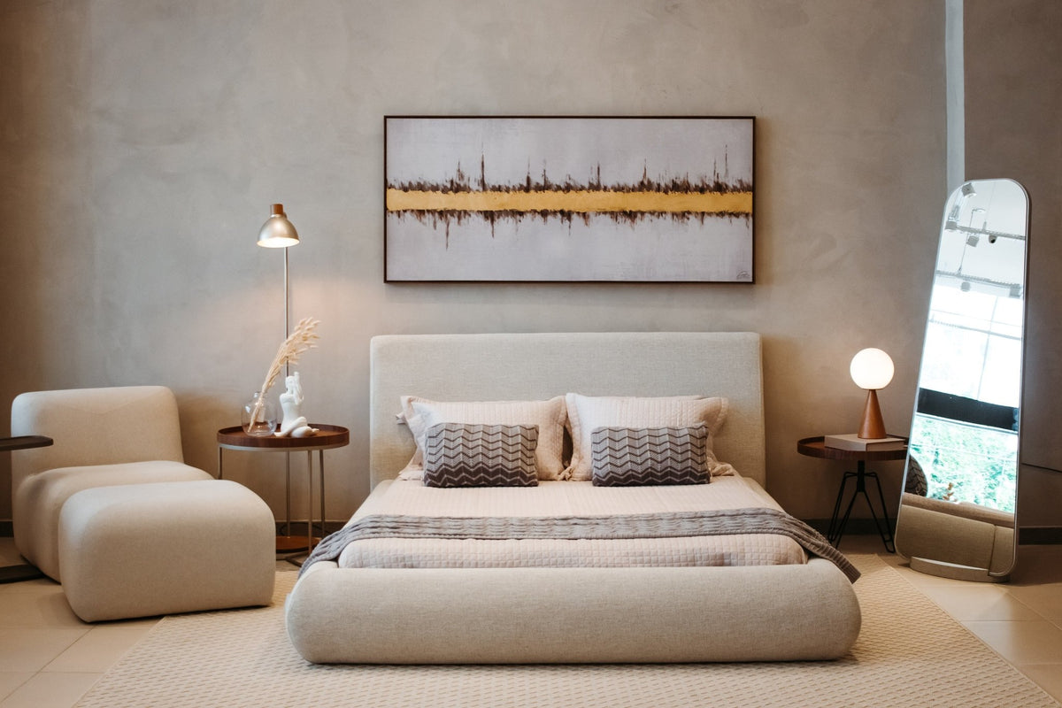 Espelho de chão no canto de quarto com cama estofada, poltrona e quadro horizontal