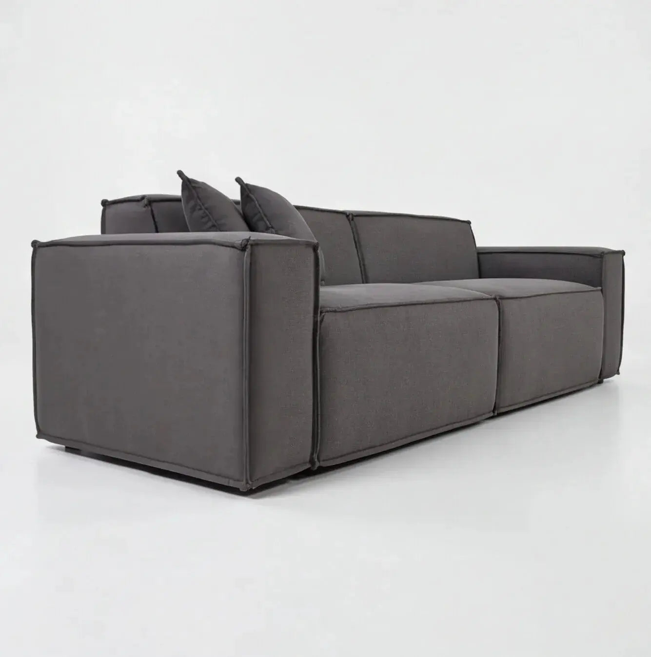 Sofá moderno cinza de três lugares com design contemporâneo e almofadas, em ambiente minimalista