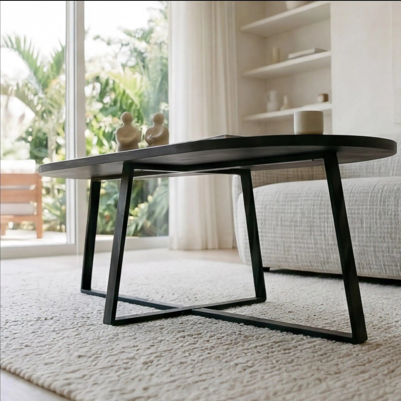 Horizon Interiores Zari black lacquered MDF coffee table with oval top and X-frame base, styled in a modern living room.