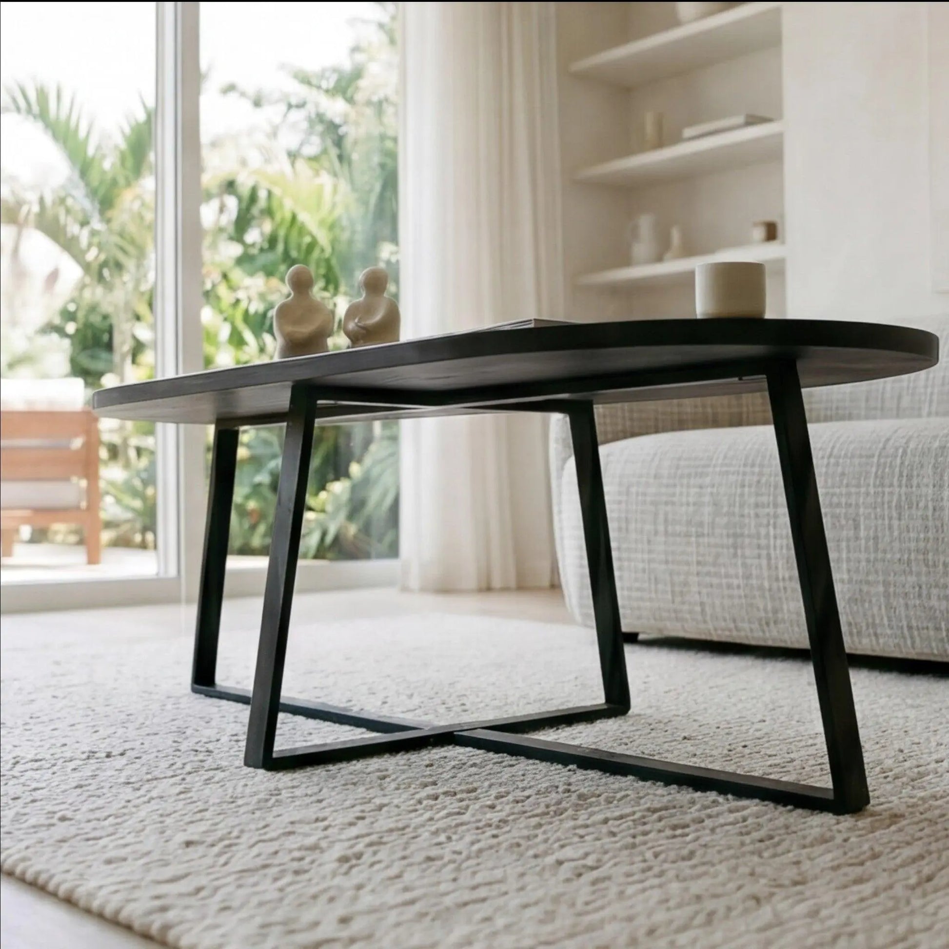 Horizon Interiores Zari black lacquered MDF coffee table with oval top and X-frame base, styled in a modern living room.