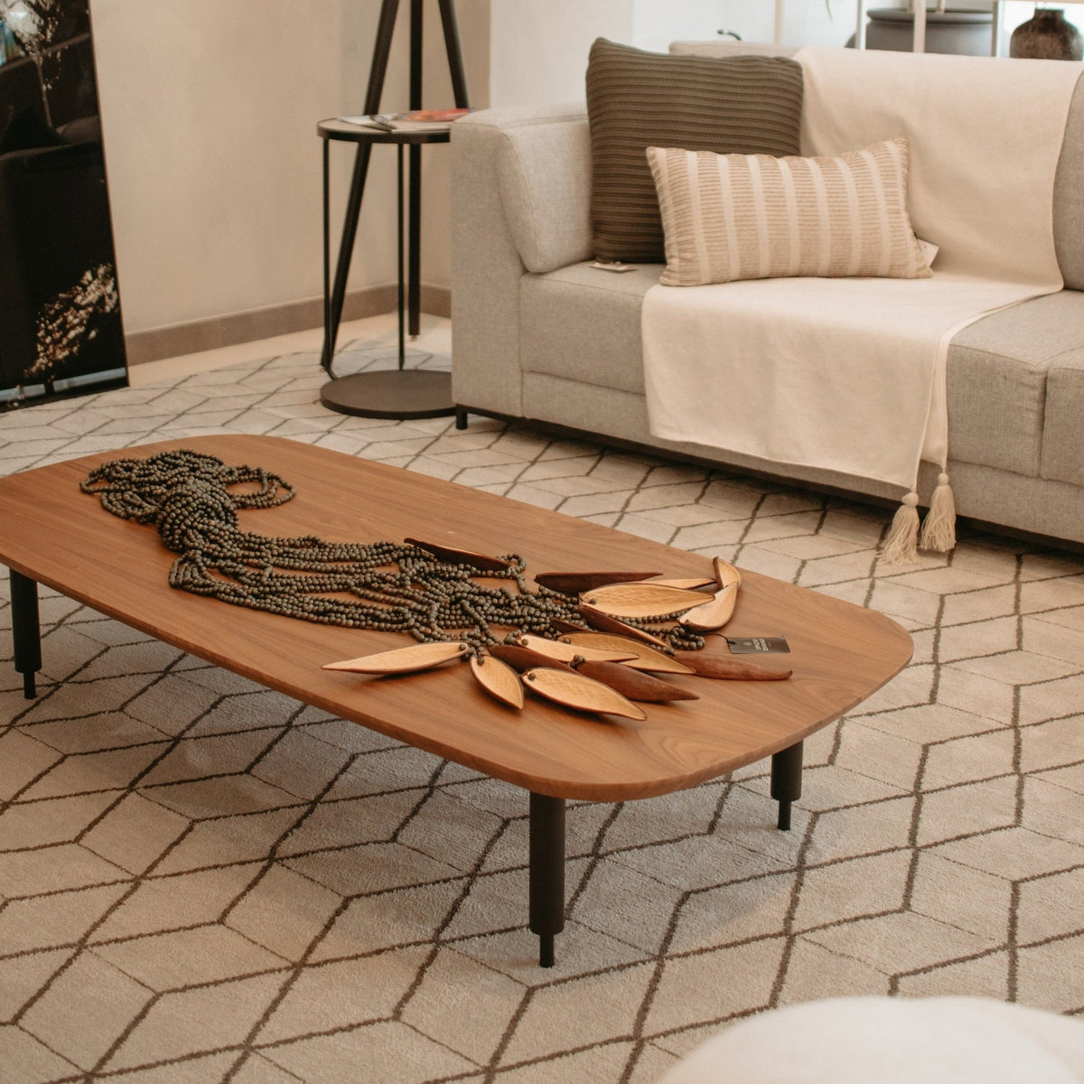 Mesa de centro alongada com peça decorativa em sala de estar com sofá, mesa lateral e tapete geométrico