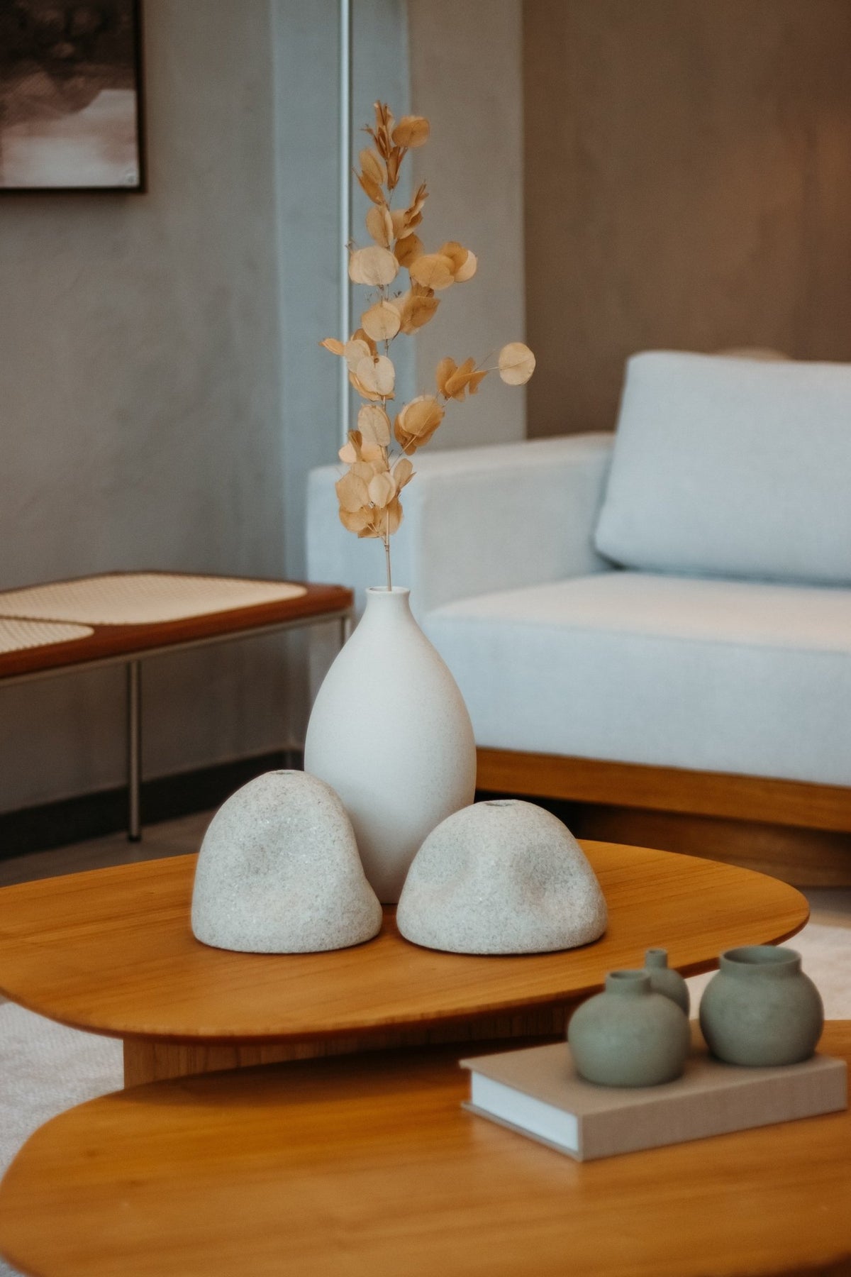 Mesa de centro de madeira com vaso de galhos secos e objetos decorativos, vista aproximada