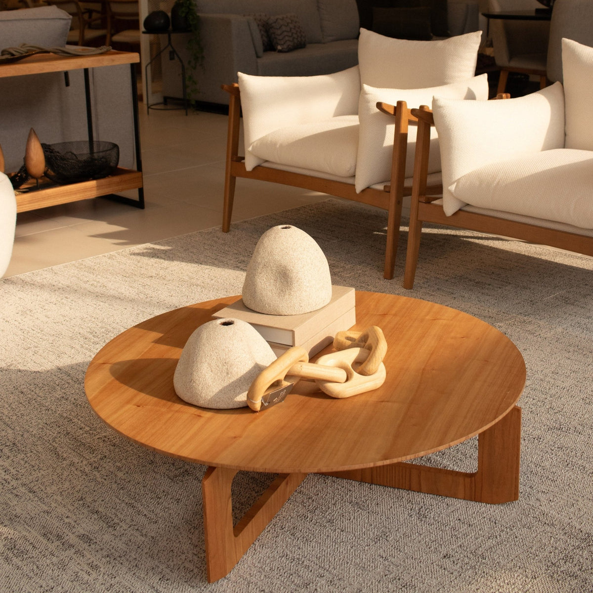 Mesa de centro redonda de madeira com base de pés cruzados em sala de estar com poltronas e tapete