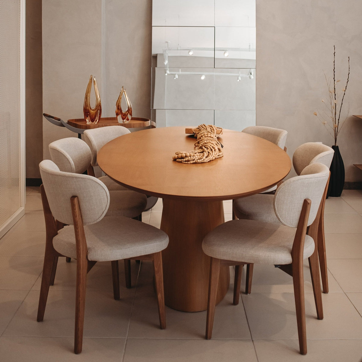 Mesa de jantar oval de madeira com peça decorativa em sala de jantar com cadeiras estofadas e vasos de vidro