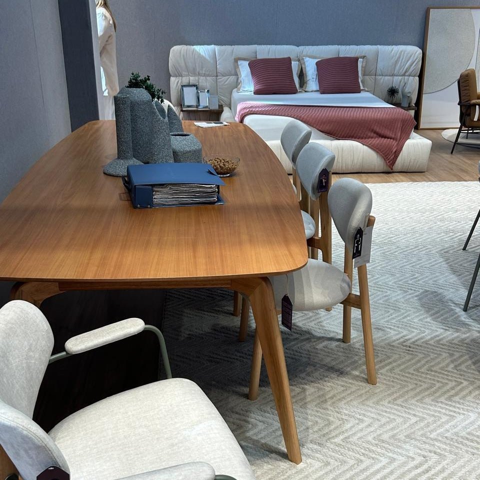 Mesa de jantar de madeira com vasos e pasta sobre o tampo em showroom com cadeiras estofadas e tapete